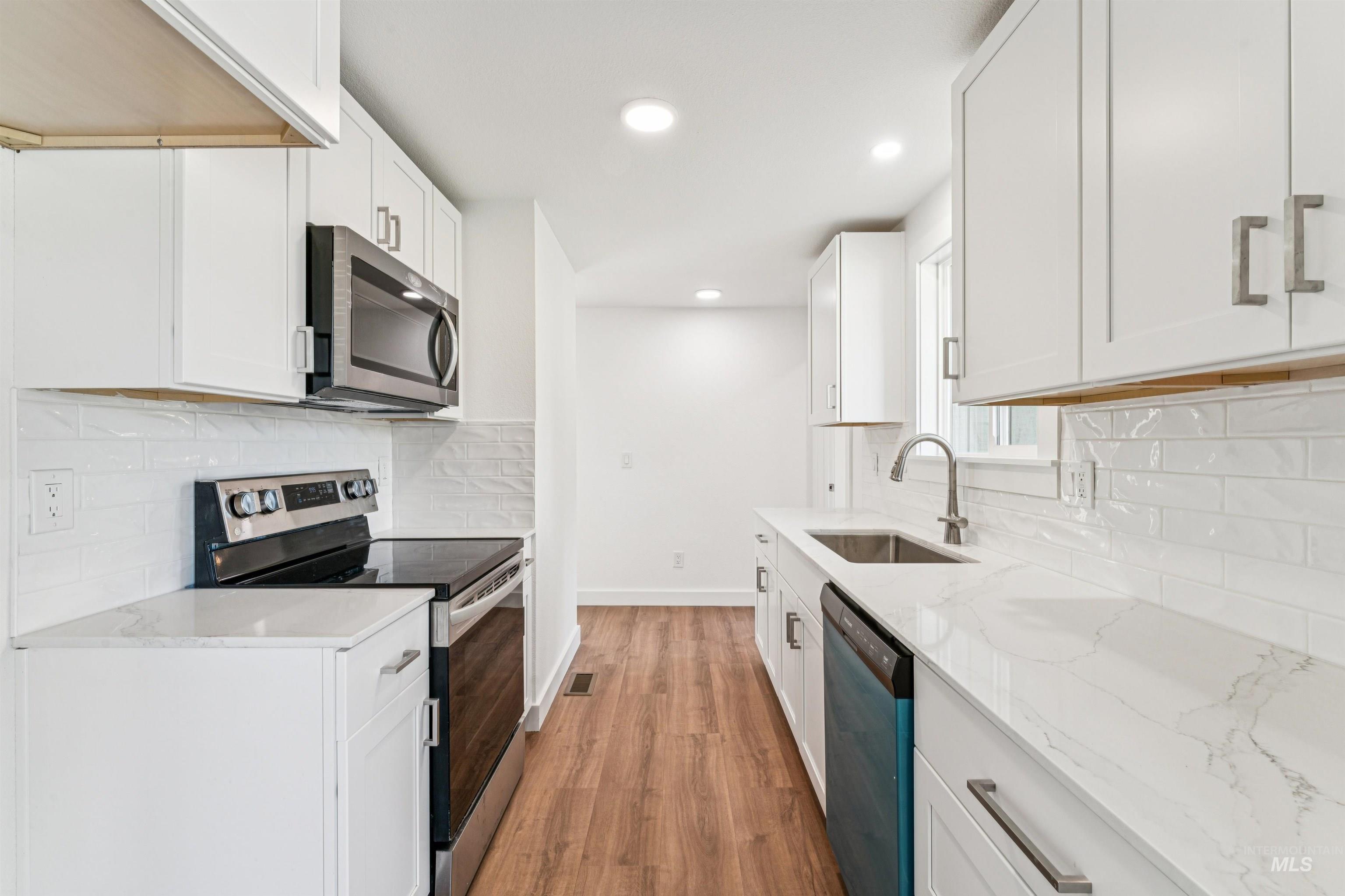 Kitchen with decorative backsplash, appliances with stainless steel finishes, light stone countertops, light wood-style flooring, and white cabinetry