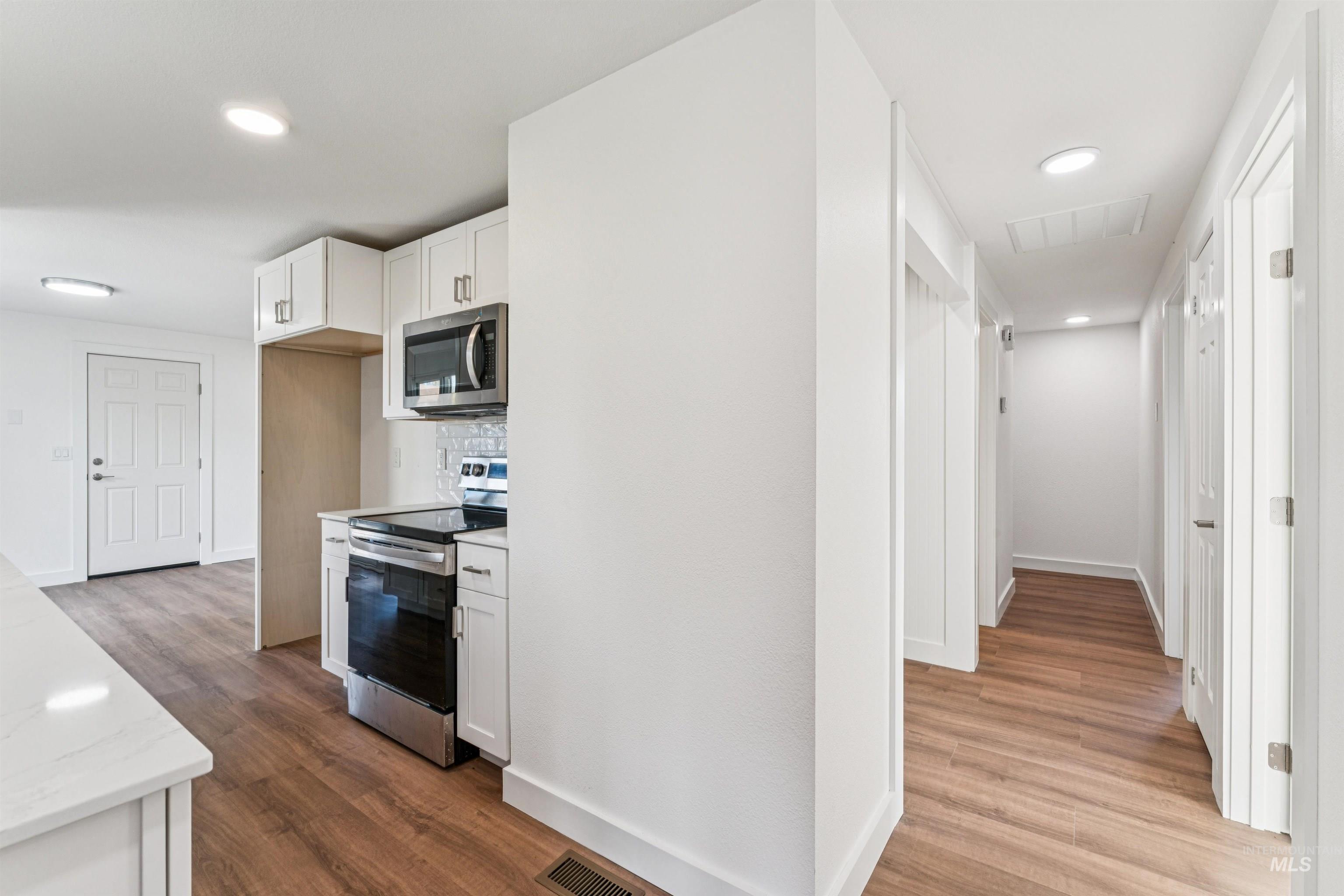 Kitchen featuring white cabinetry, stainless steel appliances, dark wood-style floors, decorative backsplash, and recessed lighting