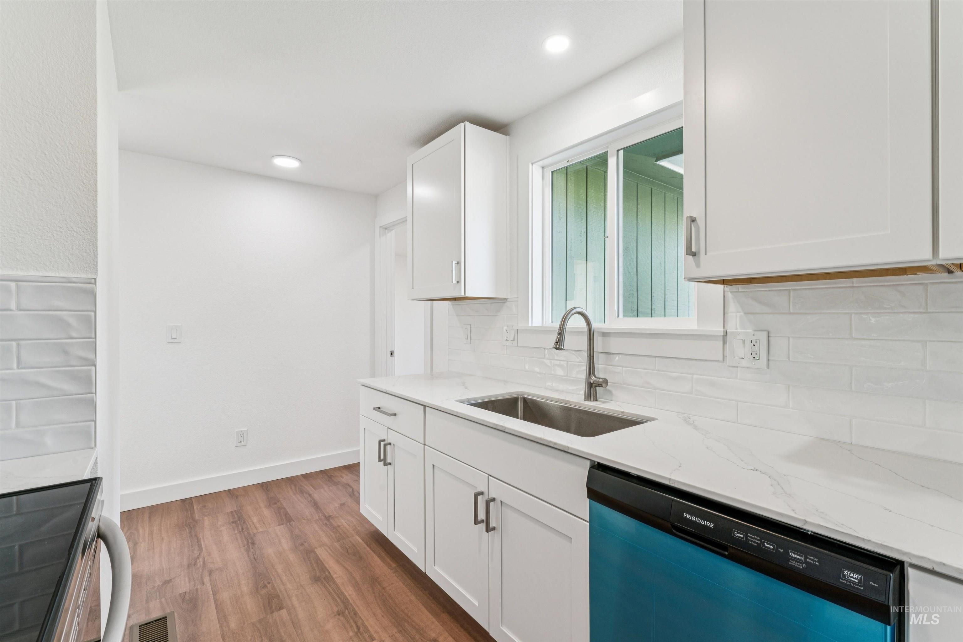 Kitchen featuring stainless steel electric stove, dishwashing machine, dark wood-style flooring, white cabinets, and light stone countertops