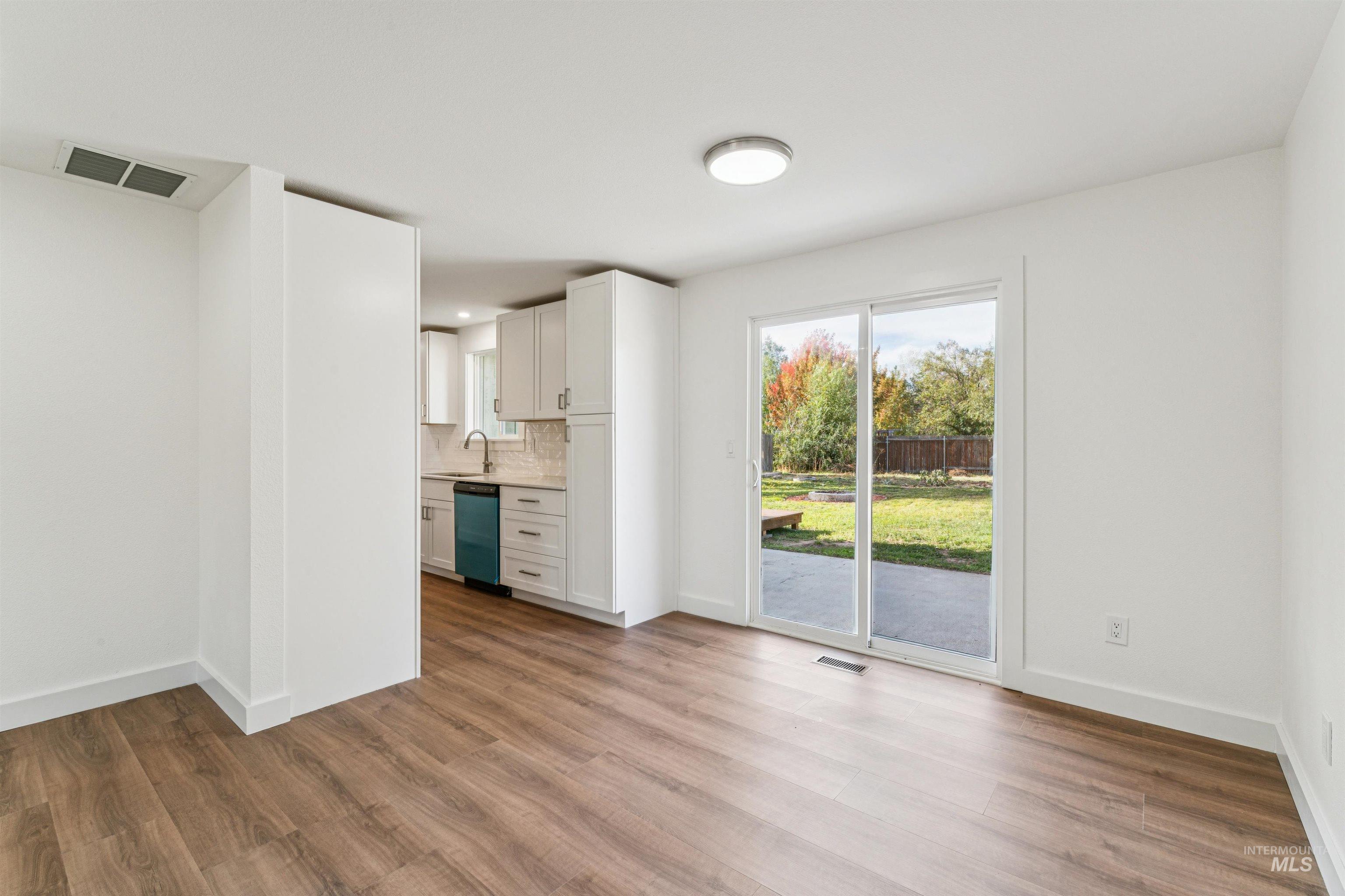 Kitchen with white cabinets, decorative backsplash, light countertops, light wood-style flooring, and dishwasher
