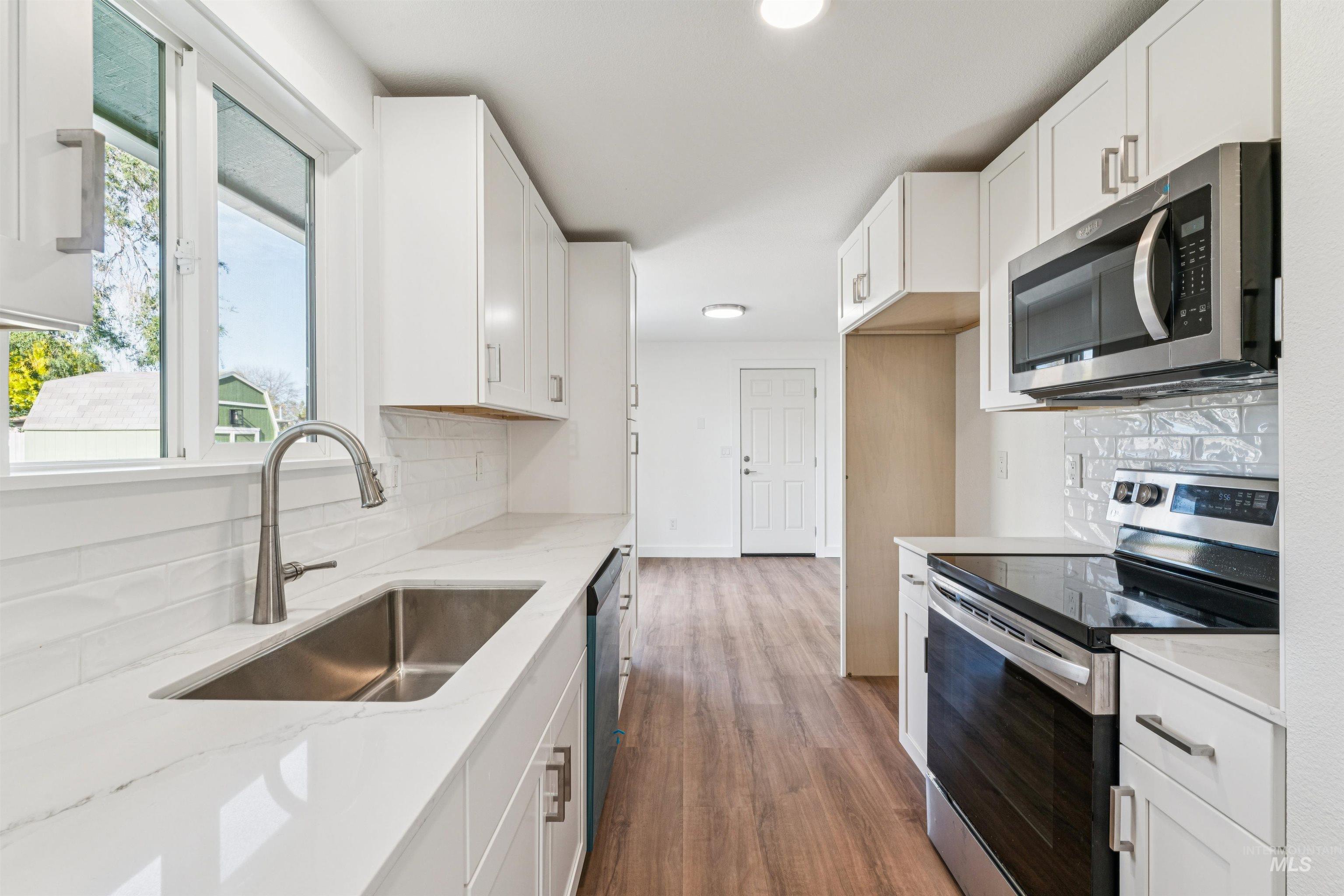 Kitchen with appliances with stainless steel finishes, tasteful backsplash, white cabinetry, dark wood finished floors, and light stone countertops