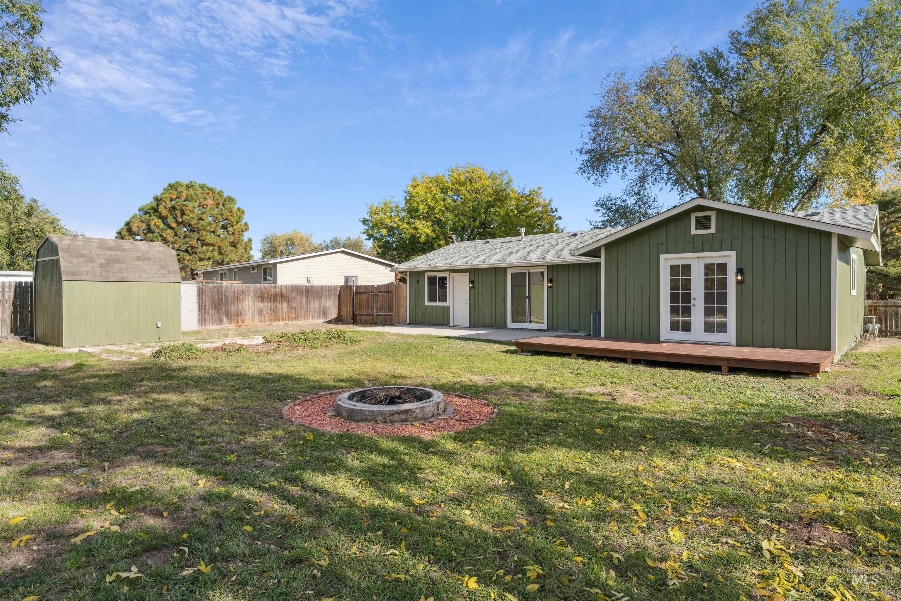 Rear view of house featuring a fire pit, a storage unit, a fenced backyard, a shingled roof, and french doors