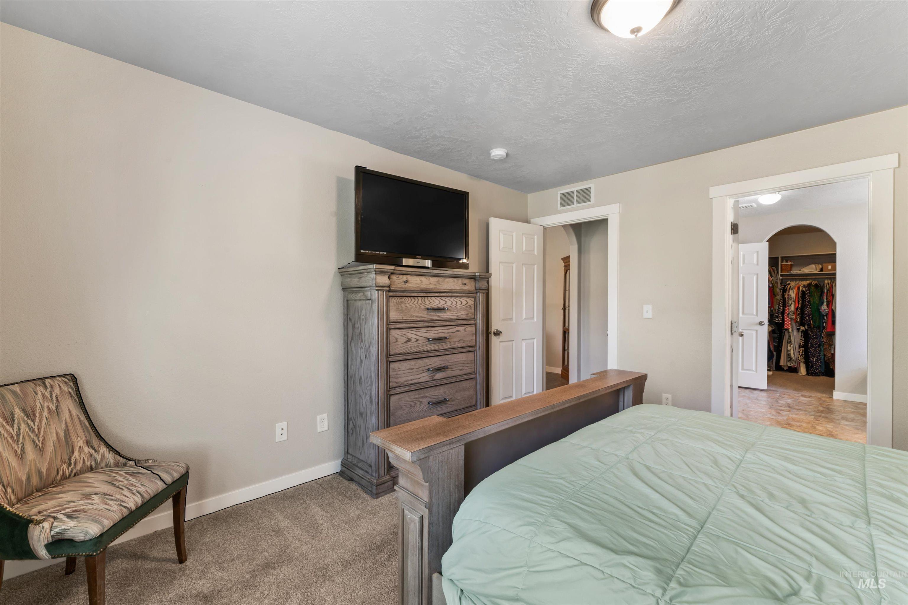 Bedroom with arched walkways, light colored carpet, a spacious closet, and a textured ceiling