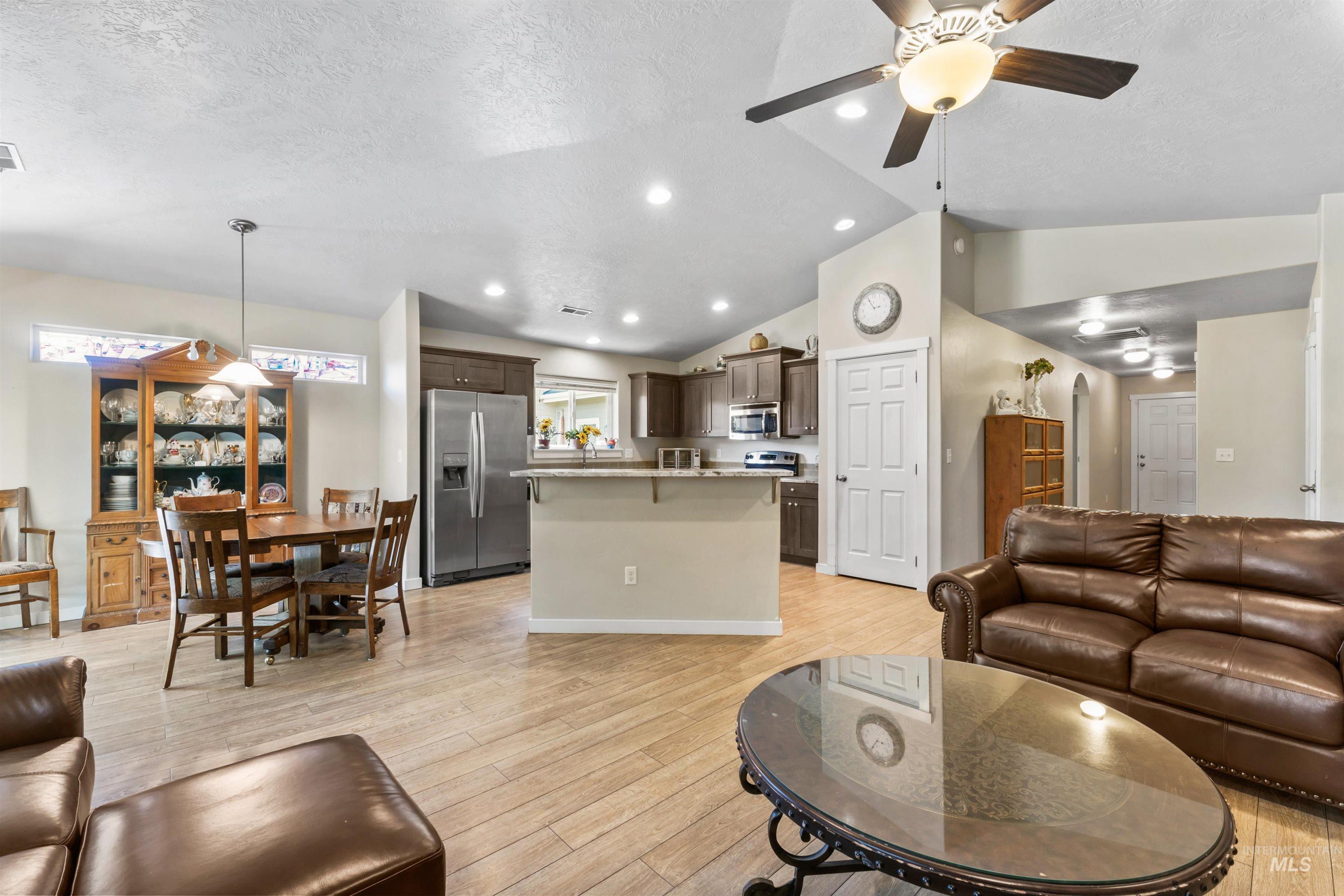 Living room with ceiling fan, light wood-style flooring, lofted ceiling, a textured ceiling, and recessed lighting