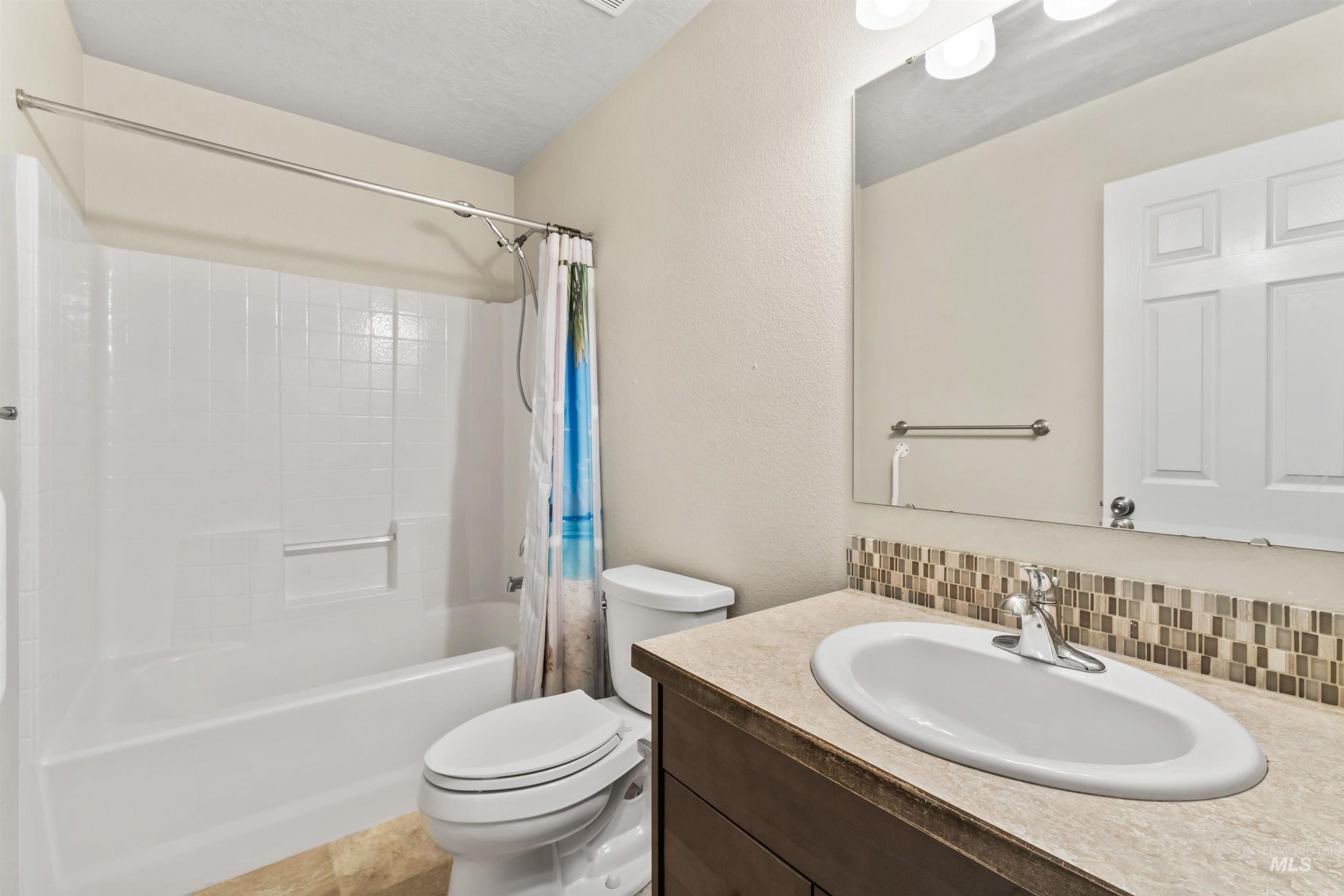 Bathroom with tasteful backsplash, vanity, shower / bath combo, and a textured wall