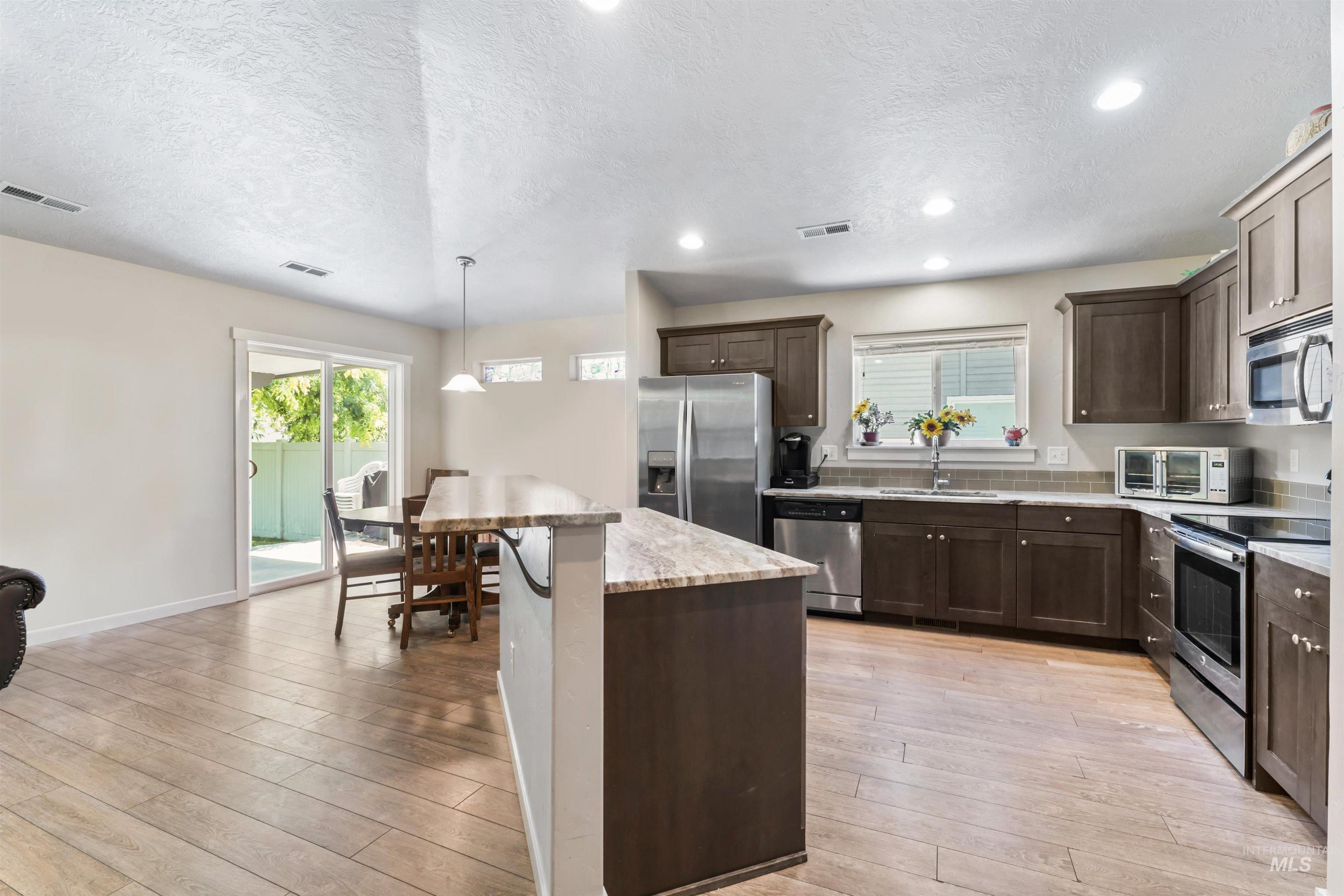 Kitchen featuring stainless steel appliances, a textured ceiling, dark brown cabinets, a center island, and light wood-type flooring