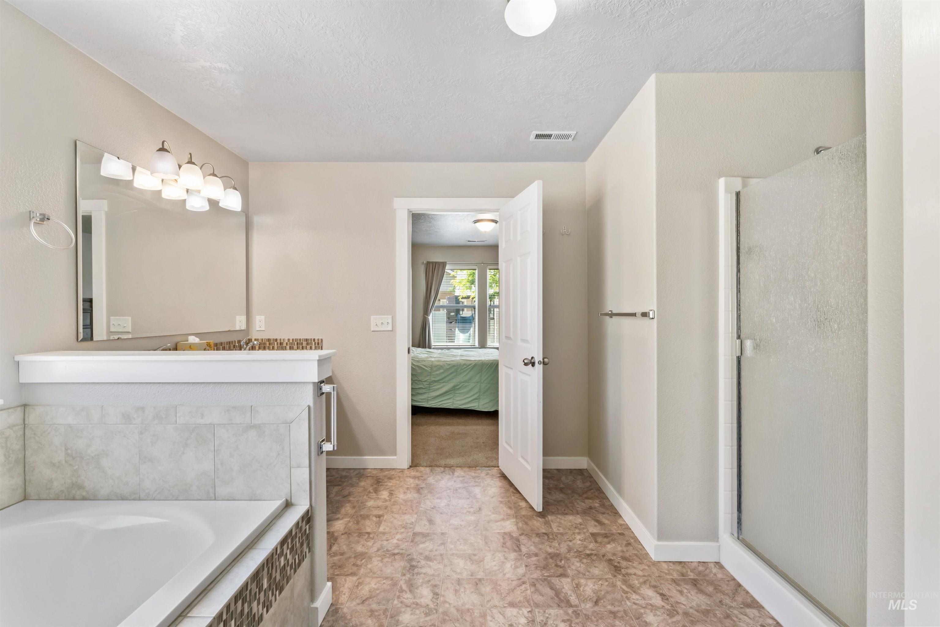 Bathroom with a stall shower, a garden tub, vanity, a textured ceiling, and ensuite bathroom