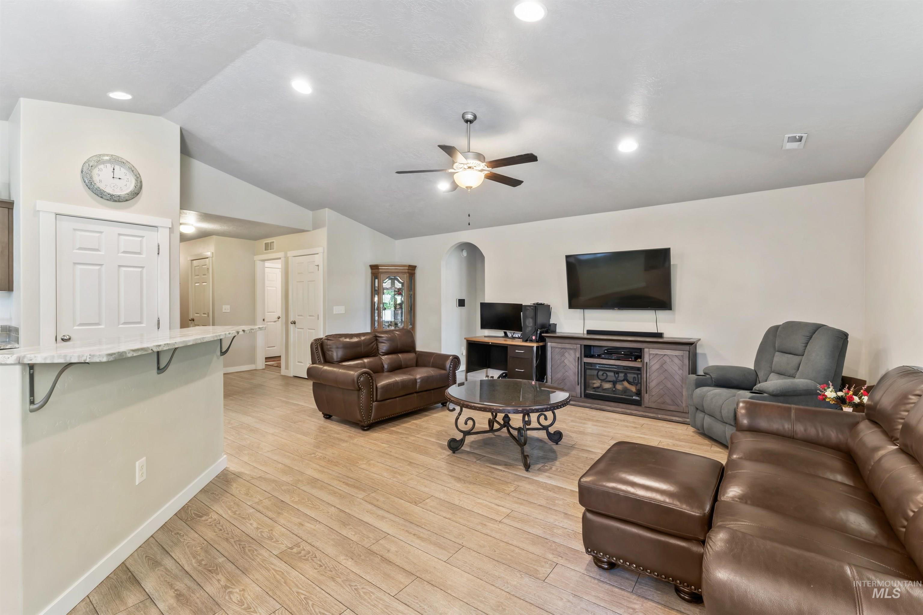 Living room featuring lofted ceiling, ceiling fan, light wood finished floors, recessed lighting, and arched walkways