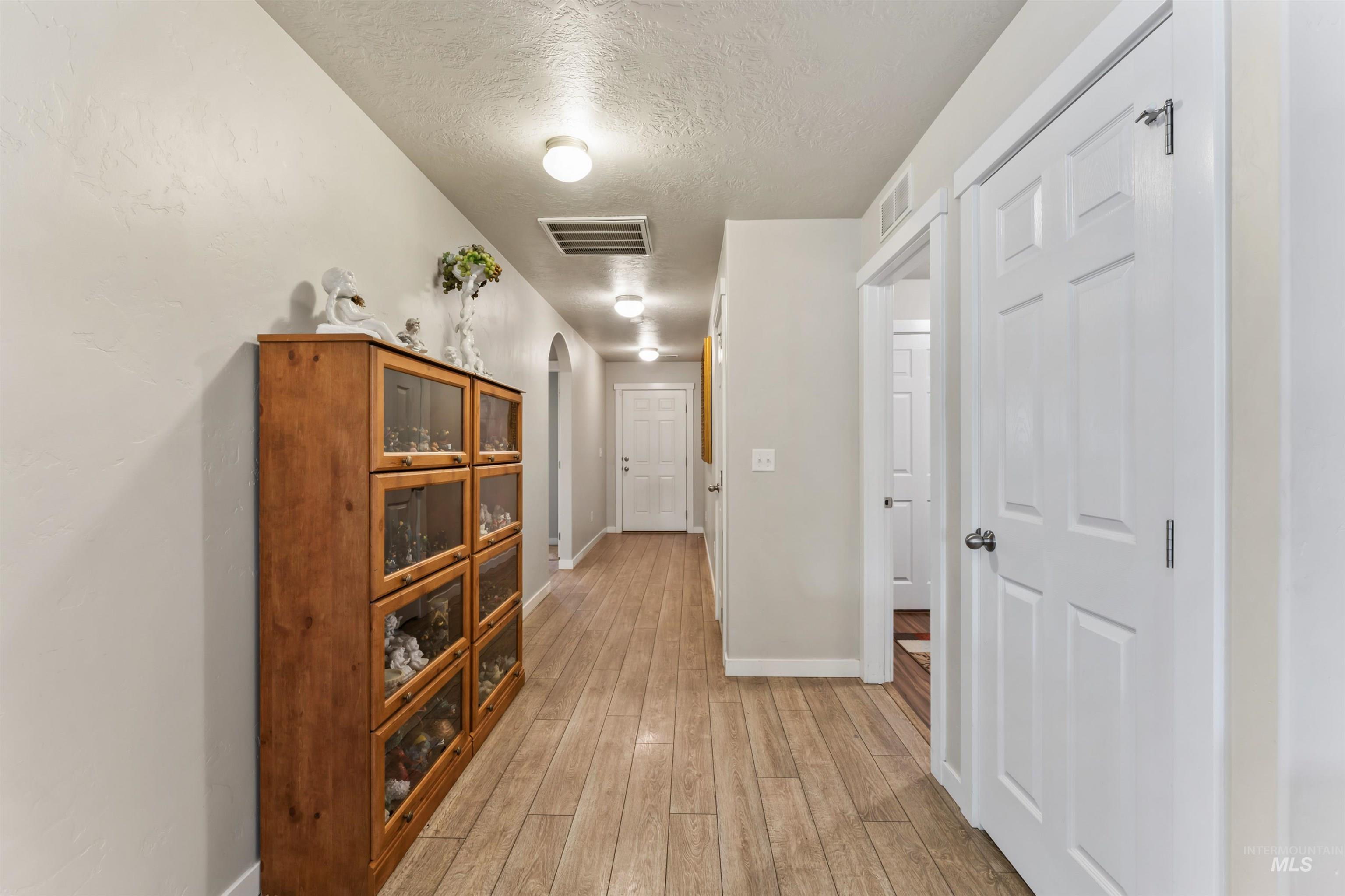Corridor with a textured ceiling, light wood-type flooring, and arched walkways