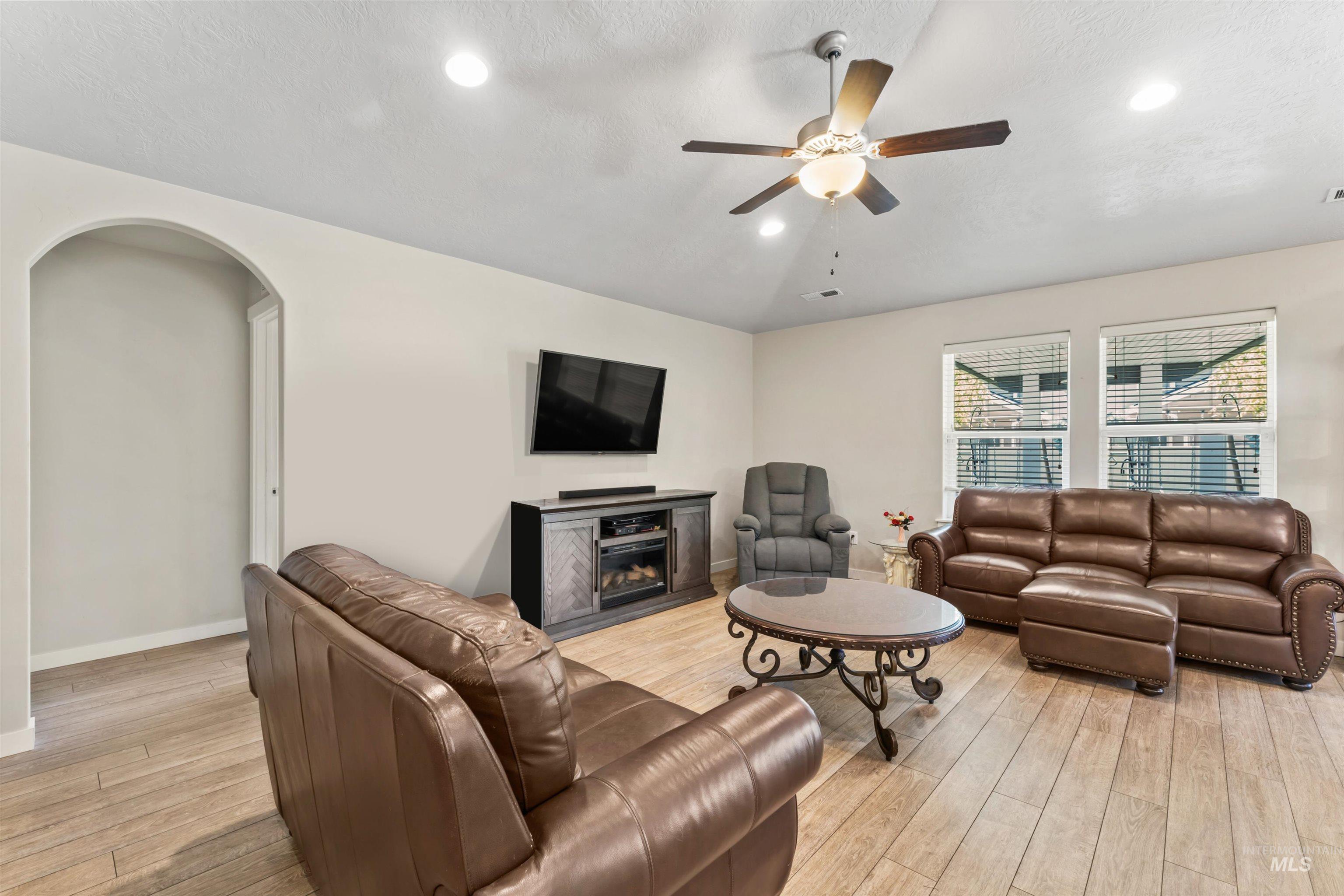 Living room featuring ceiling fan, light wood-type flooring, arched walkways, recessed lighting, and a glass covered fireplace