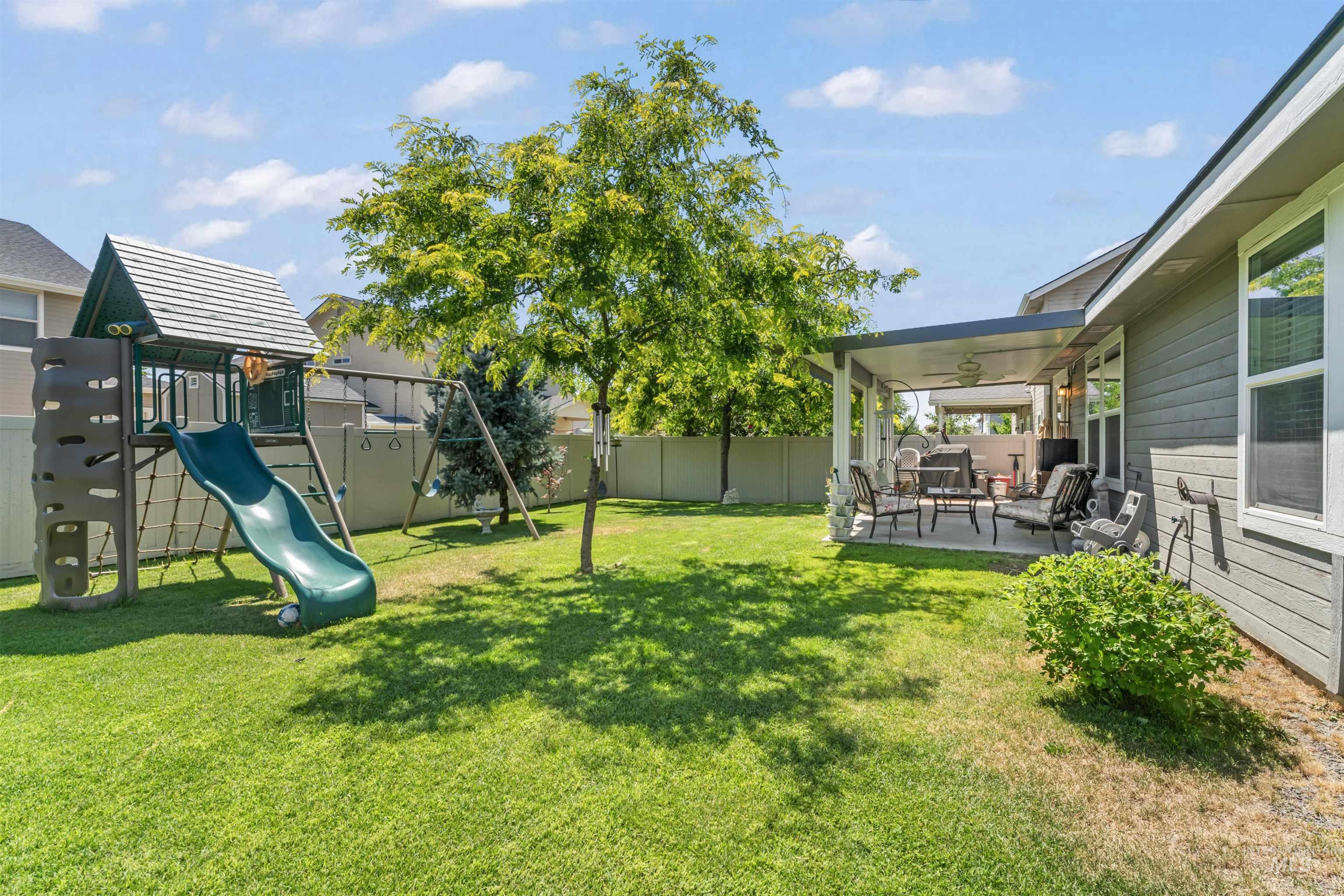 Fenced backyard featuring a patio, a playground, and a ceiling fan