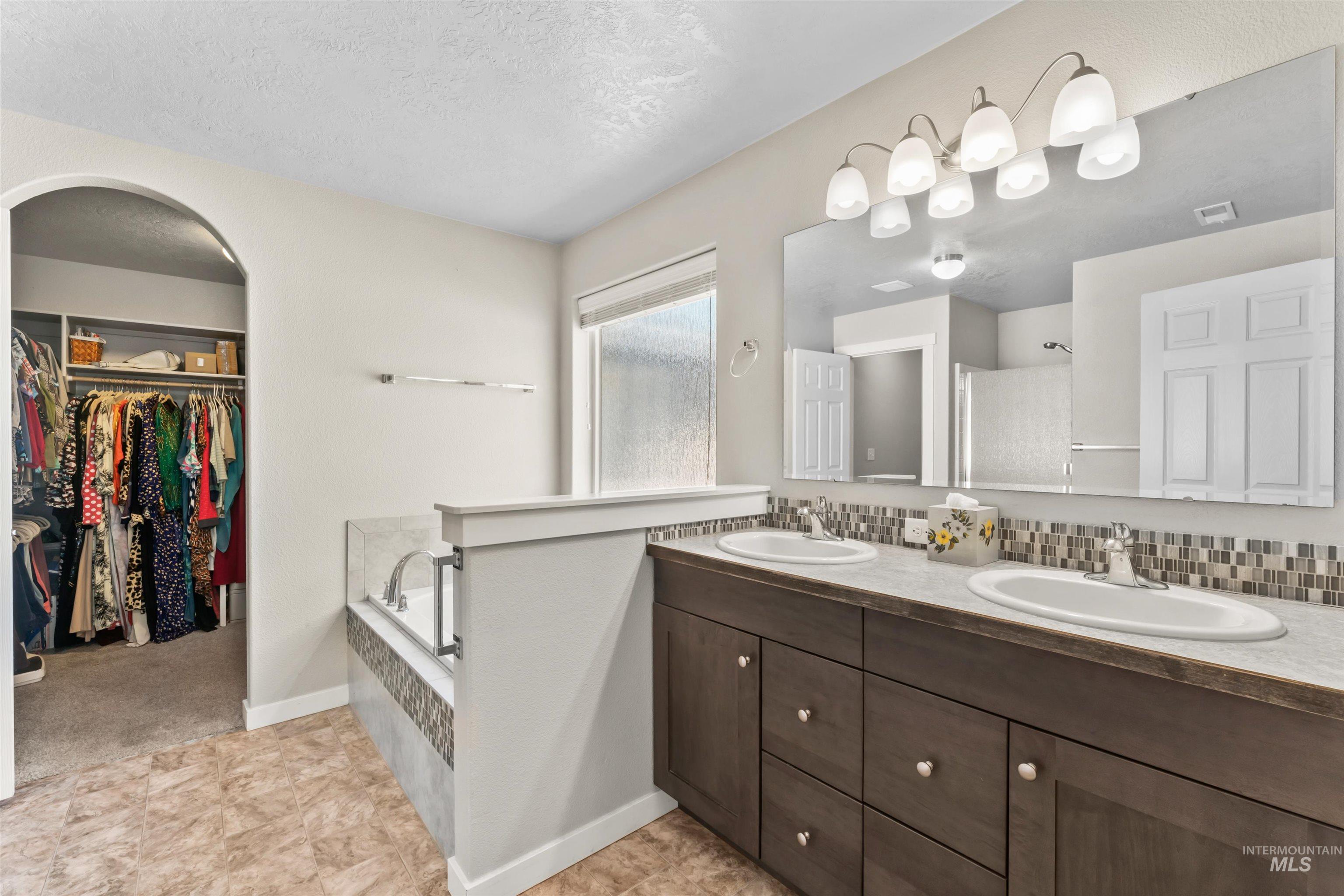 Bathroom featuring double vanity, a bath, a spacious closet, a textured ceiling, and a shower