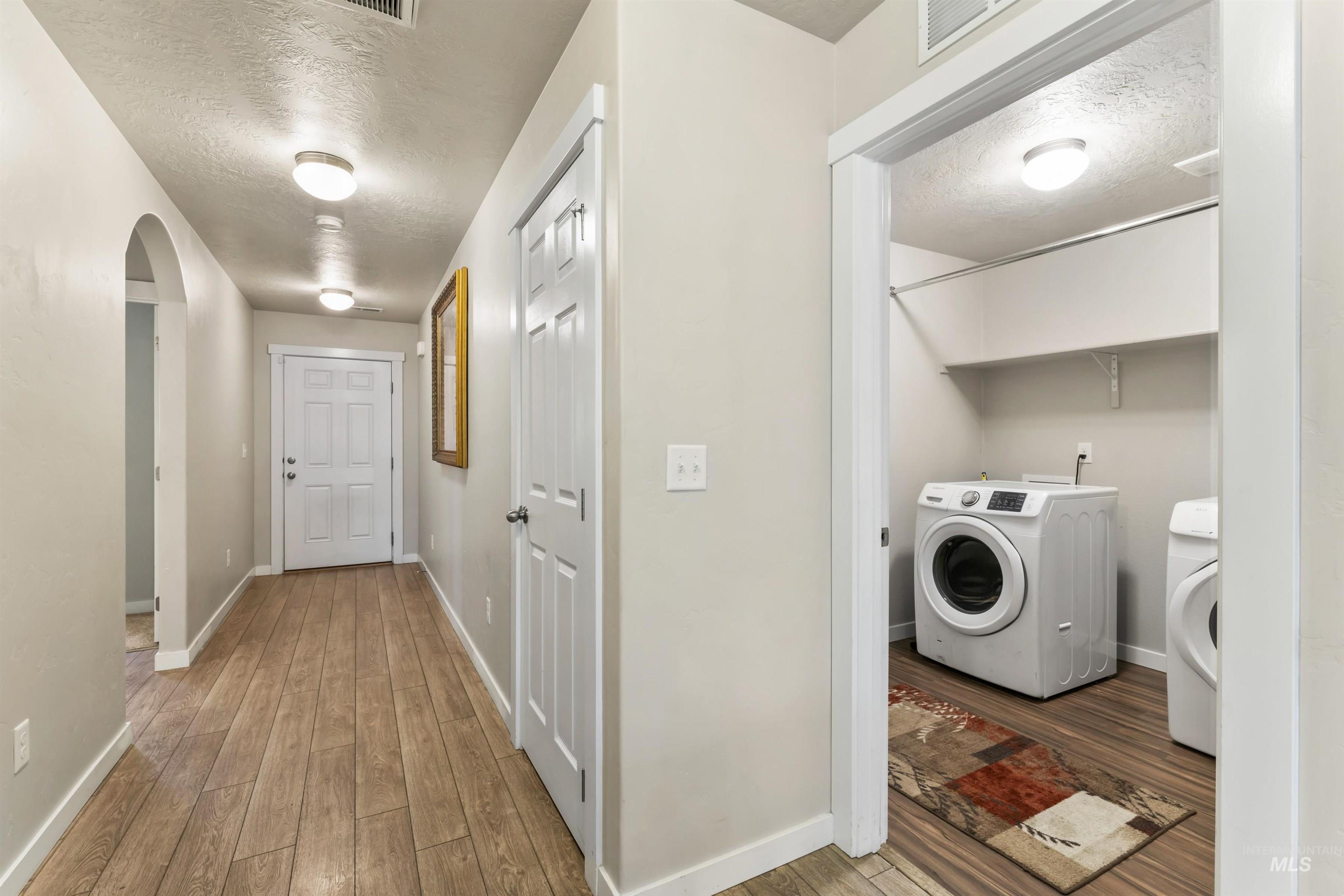 Washroom featuring a textured ceiling, wood-type flooring, arched walkways, and washer and clothes dryer