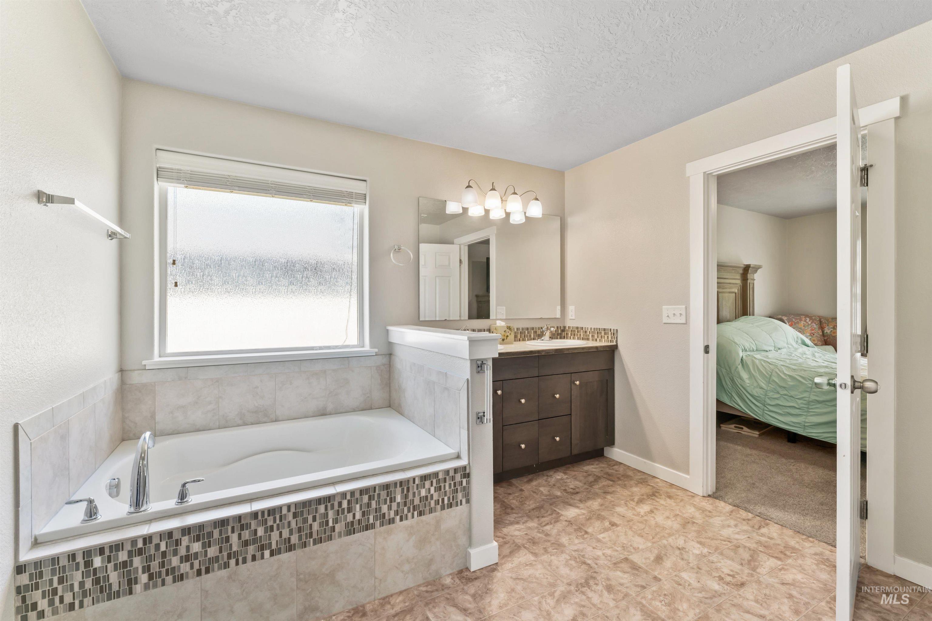 Full bath featuring vanity, a garden tub, ensuite bathroom, and a textured ceiling