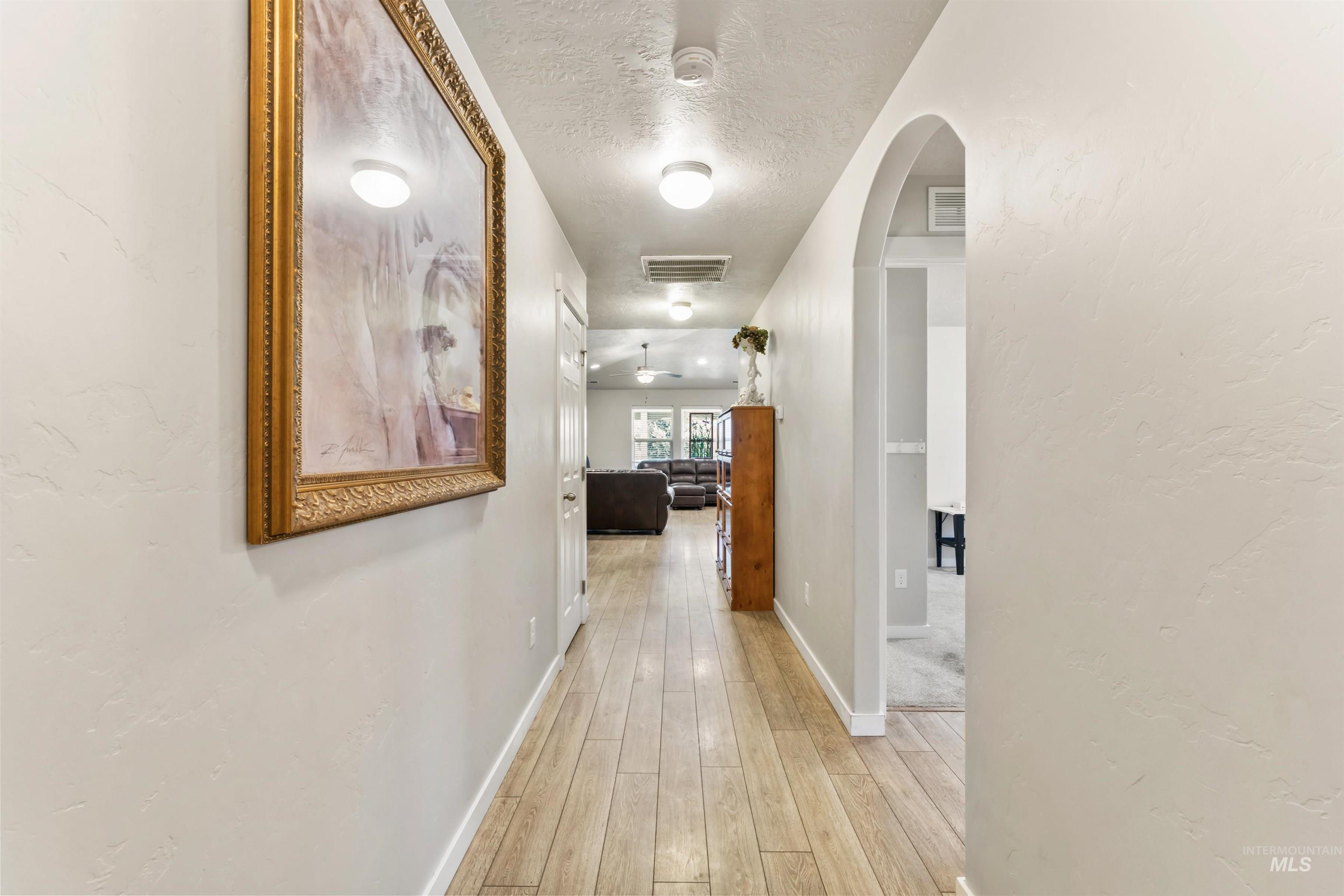 Hallway with light wood-style floors, arched walkways, and a textured ceiling
