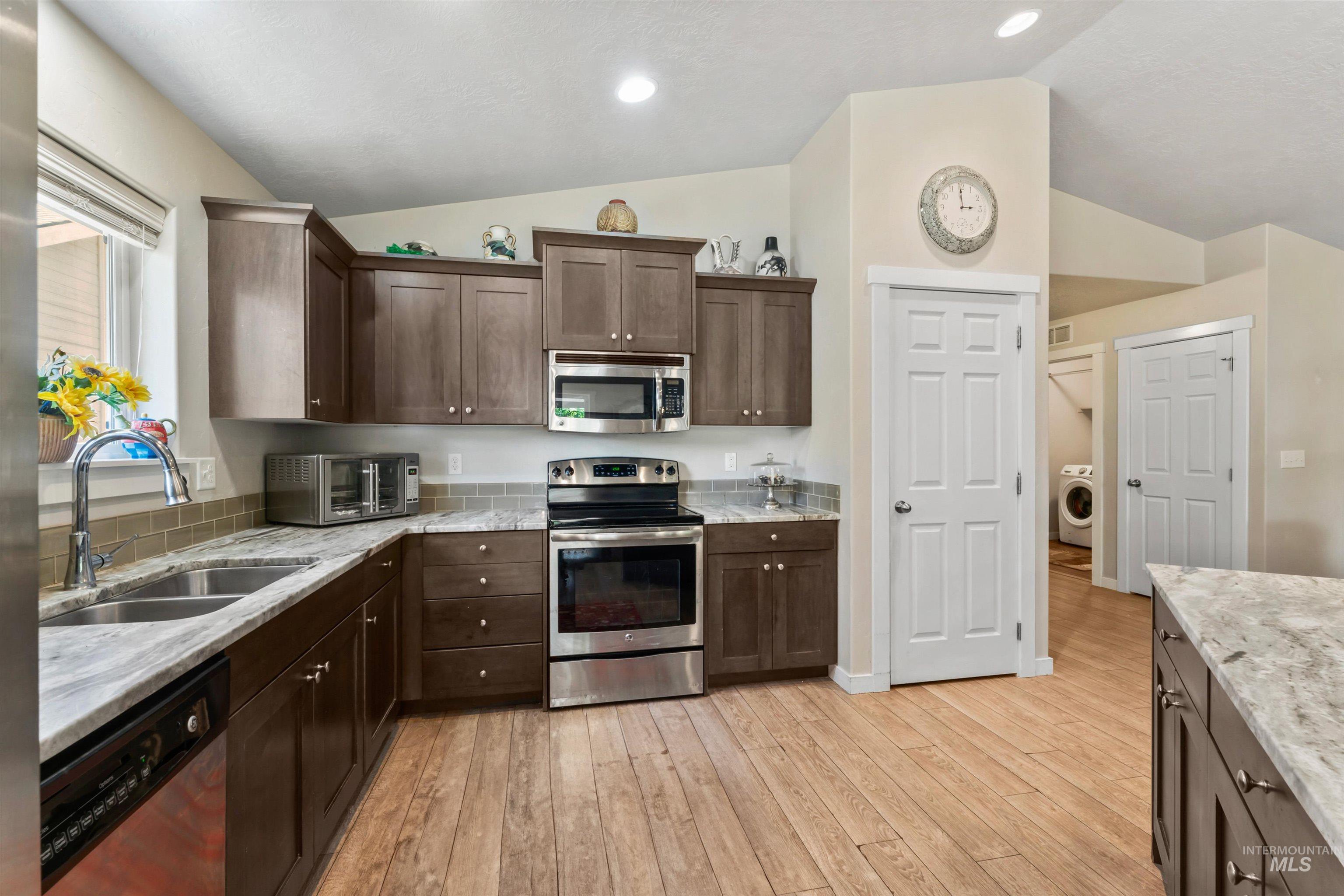 Kitchen featuring appliances with stainless steel finishes, vaulted ceiling, washer / dryer, dark brown cabinetry, and light wood finished floors