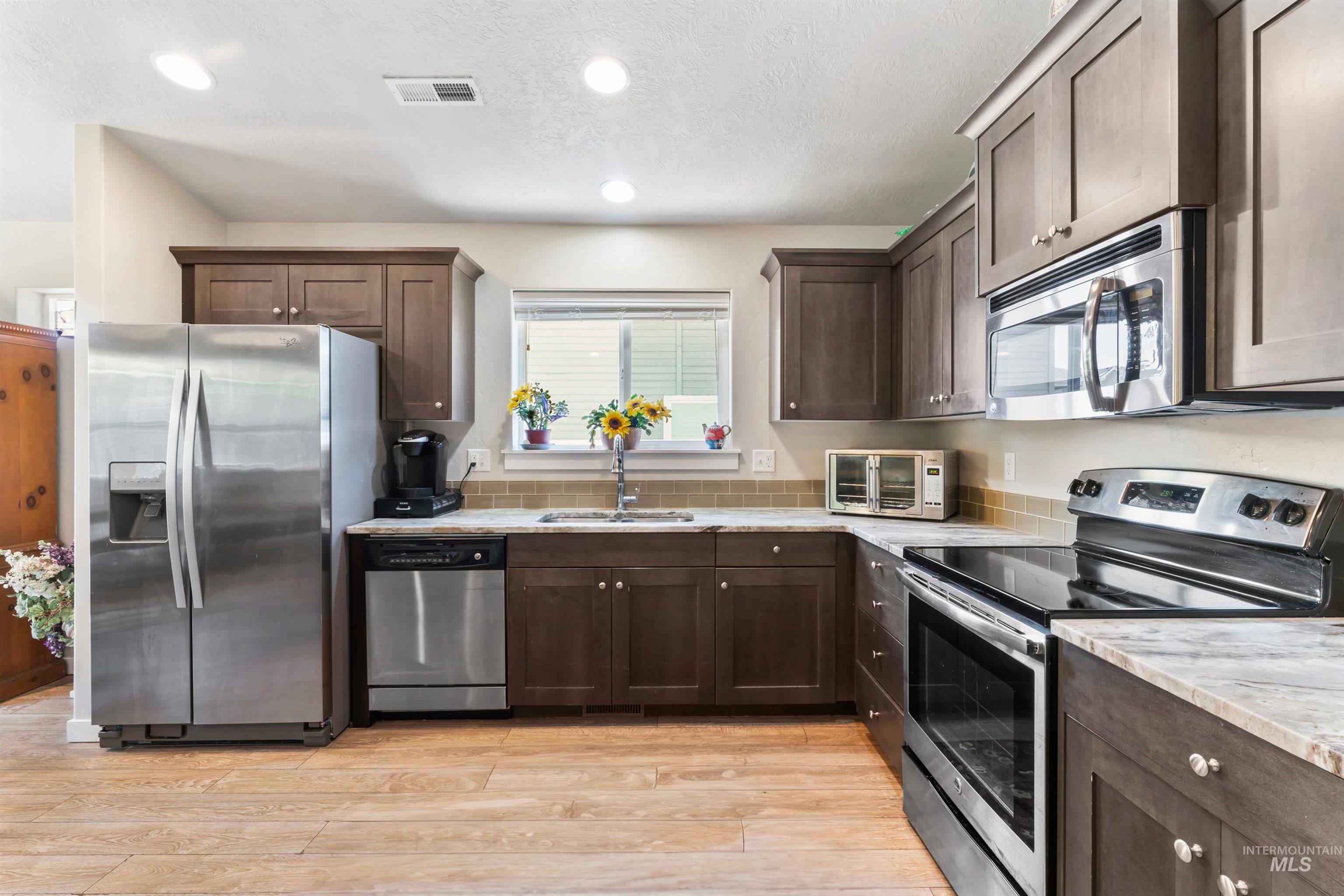 Kitchen featuring stainless steel appliances, dark brown cabinetry, light wood finished floors, light stone counters, and recessed lighting
