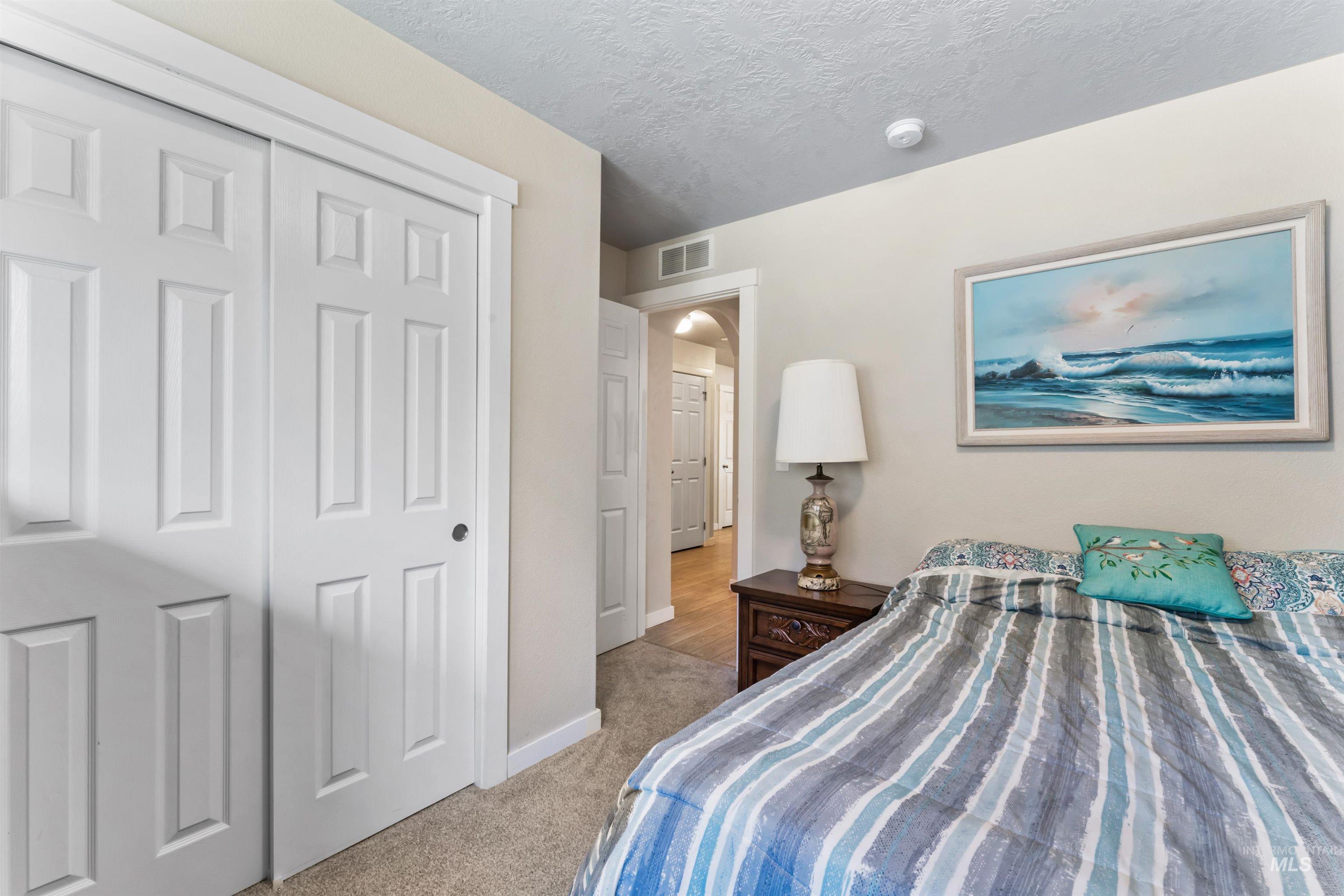 Bedroom with light colored carpet, arched walkways, a closet, and a textured ceiling