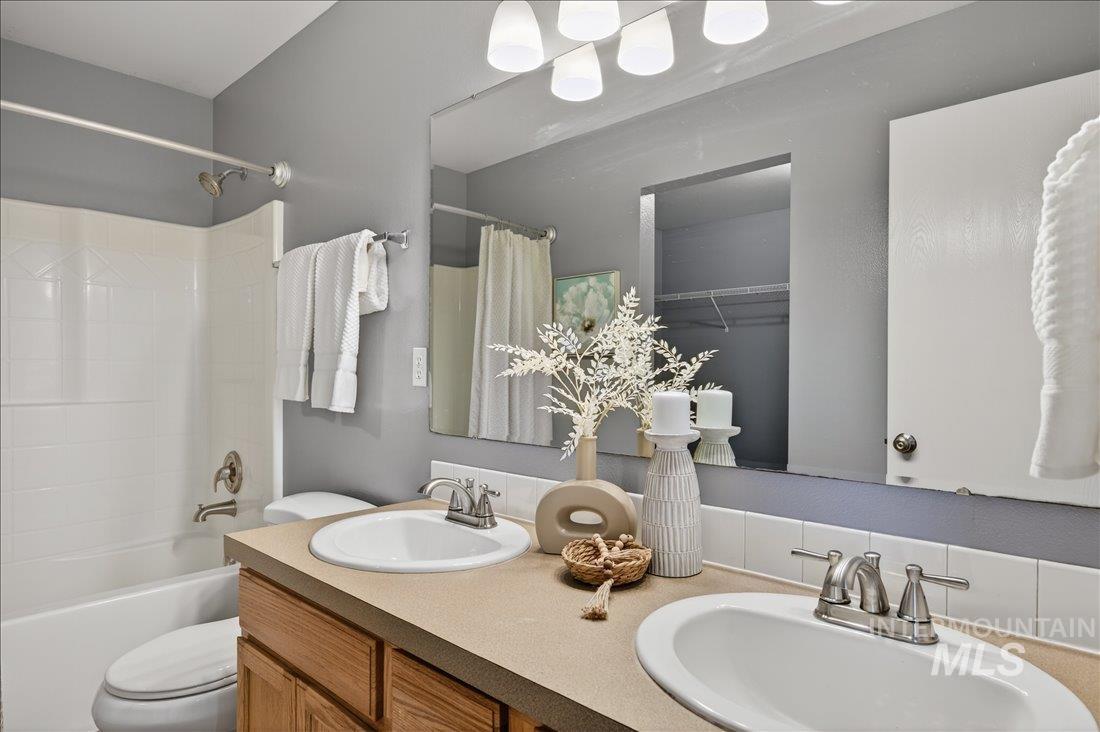 Full bath with double vanity, shower / tub combo with curtain, and a spacious closet