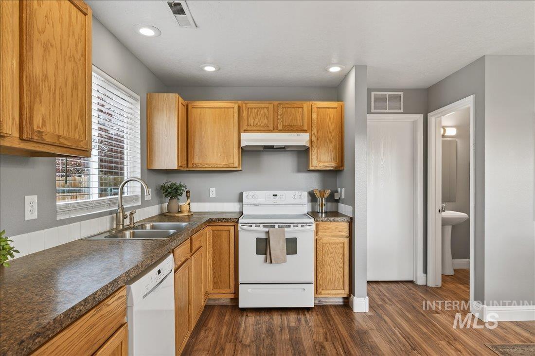 Kitchen featuring white appliances, dark wood finished floors, under cabinet range hood, recessed lighting, and dark countertops