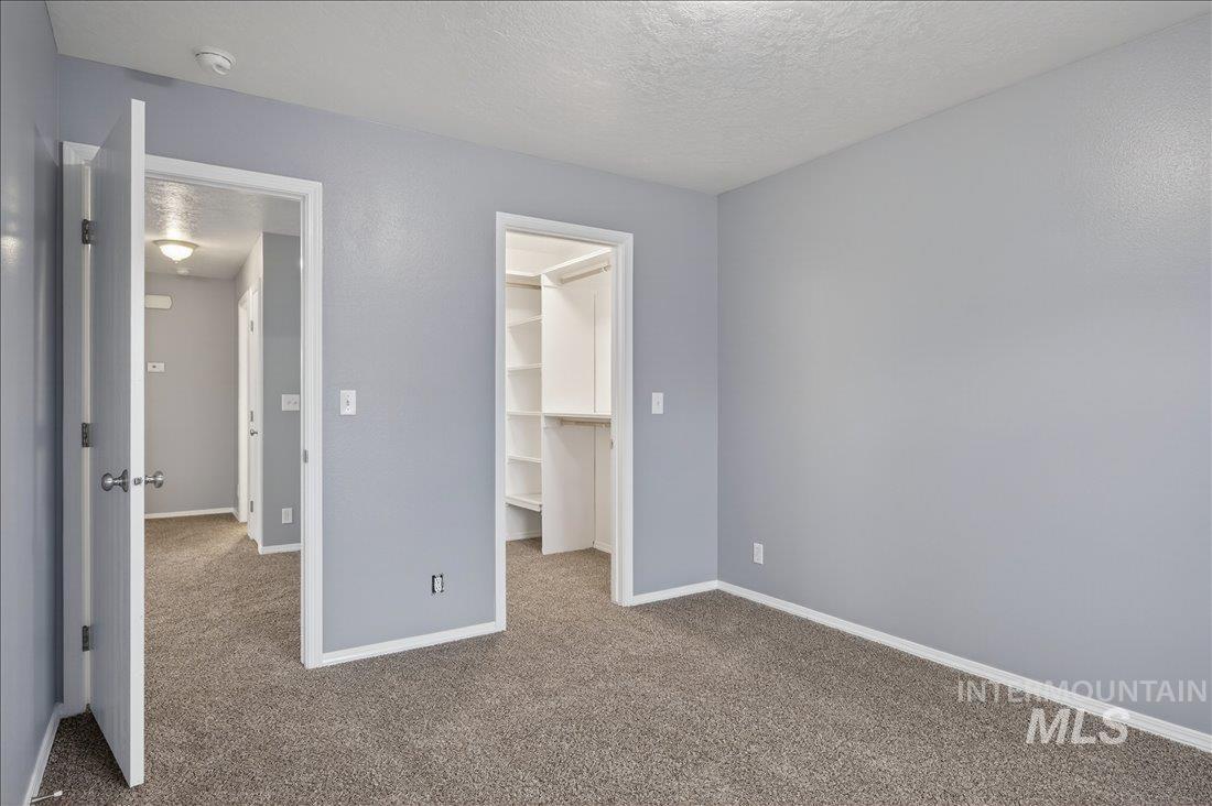 Unfurnished bedroom with a textured ceiling, carpet floors, and a walk in closet