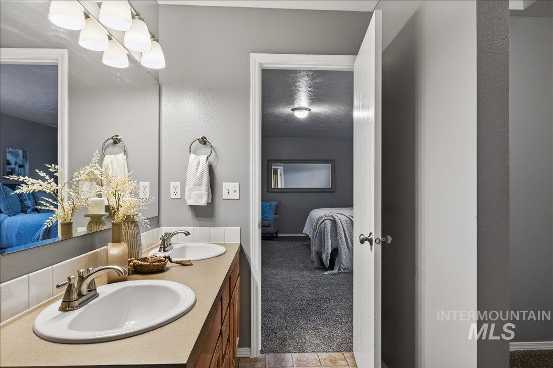 Bathroom featuring connected bathroom, light carpet, double vanity, and a textured ceiling