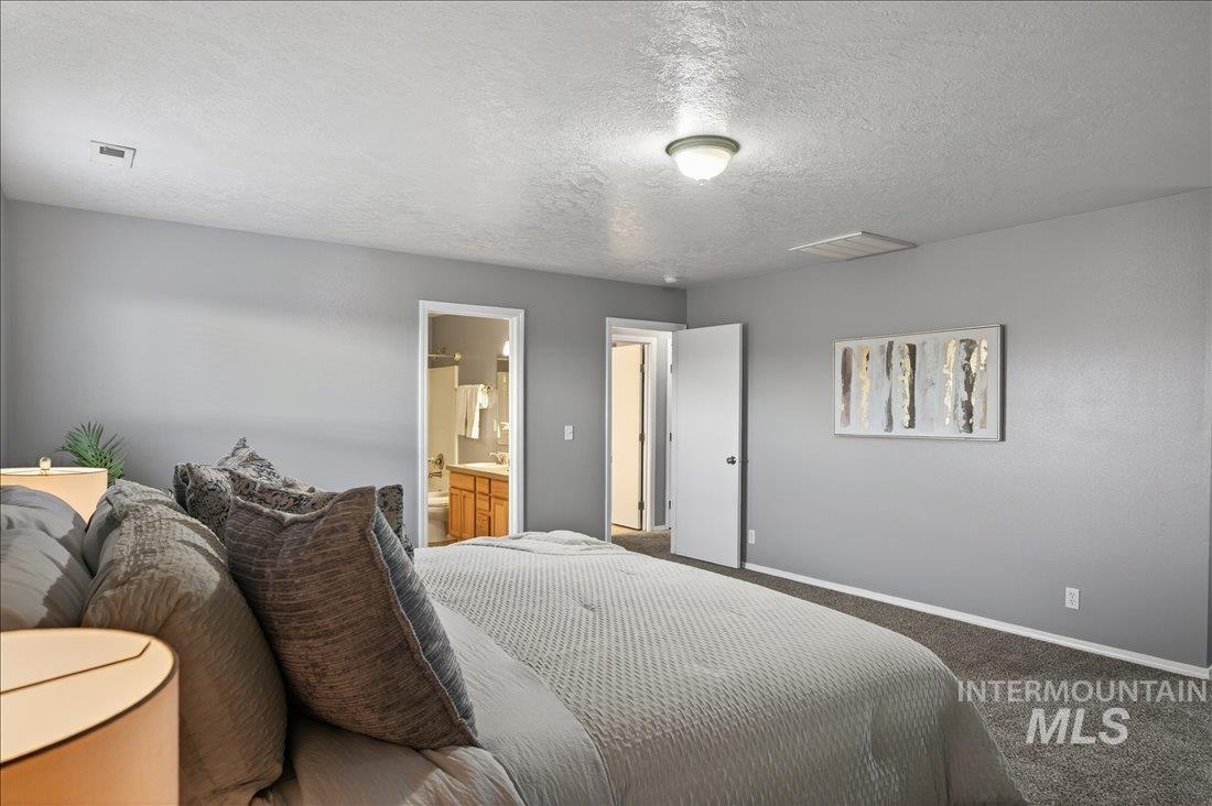 Carpeted bedroom featuring a textured ceiling and ensuite bathroom