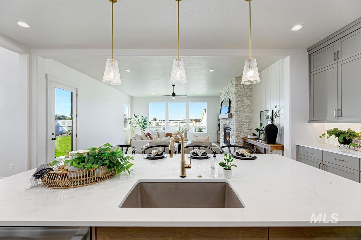 Kitchen with gray cabinetry, light stone countertops, pendant lighting, a stone fireplace, and open floor plan