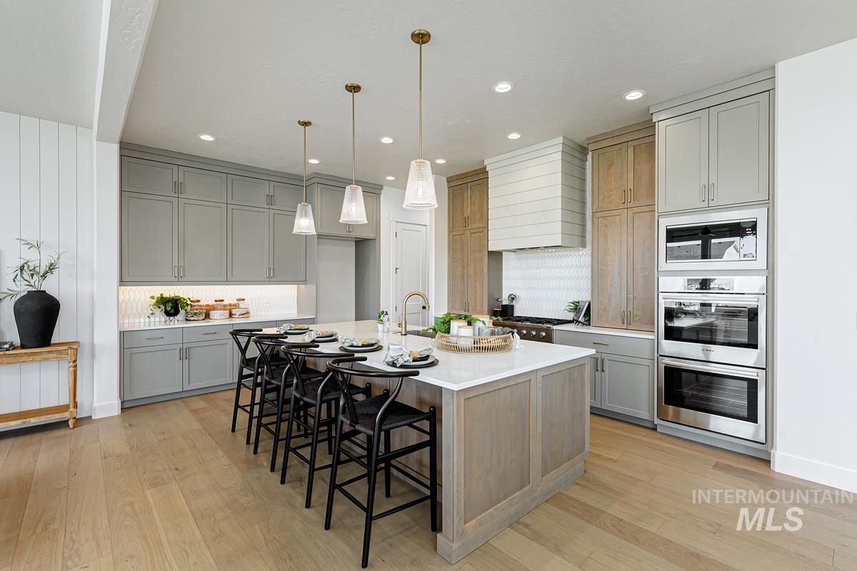 Kitchen with a kitchen bar, hanging light fixtures, gray cabinets, a center island with sink, and light stone countertops