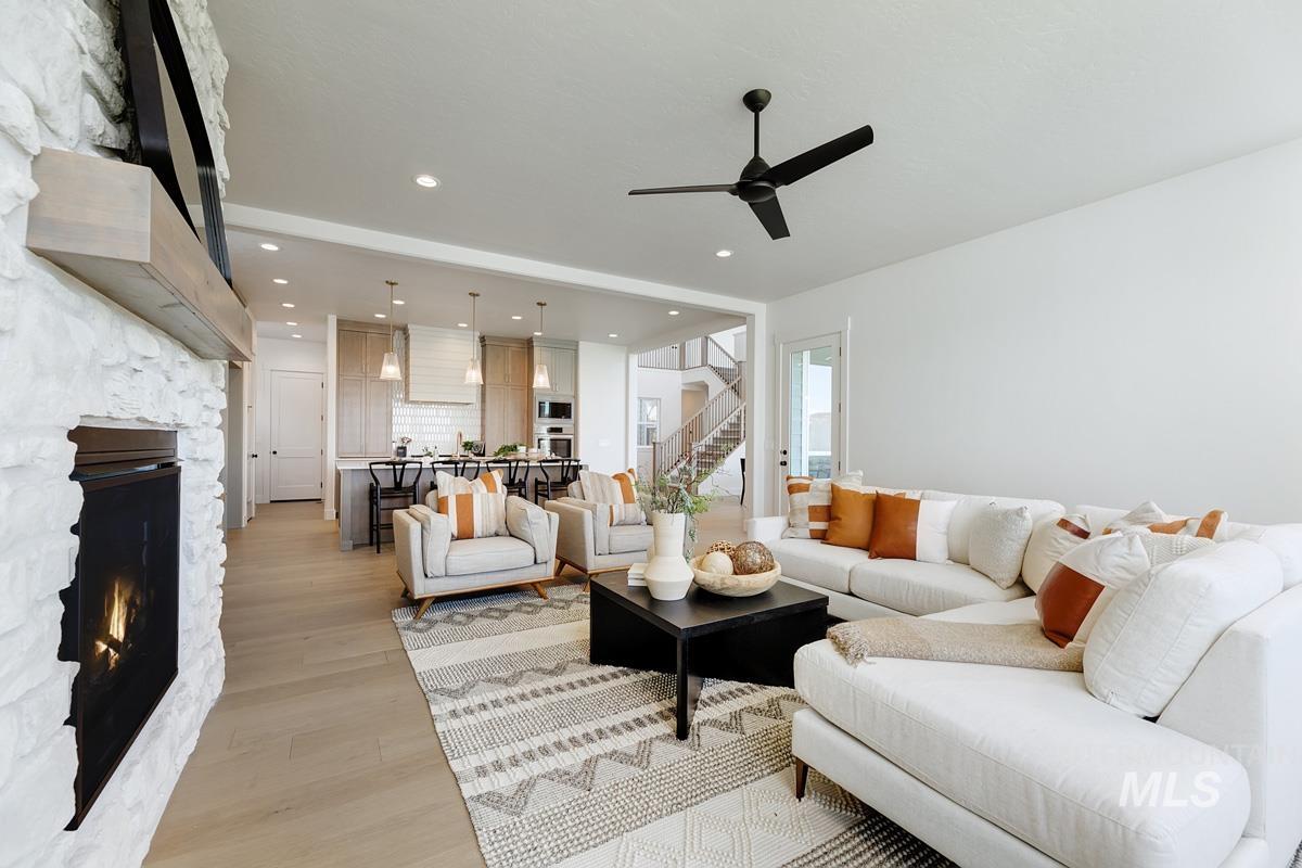 Living room featuring light wood-style flooring, stairs, a stone fireplace, recessed lighting, and ceiling fan