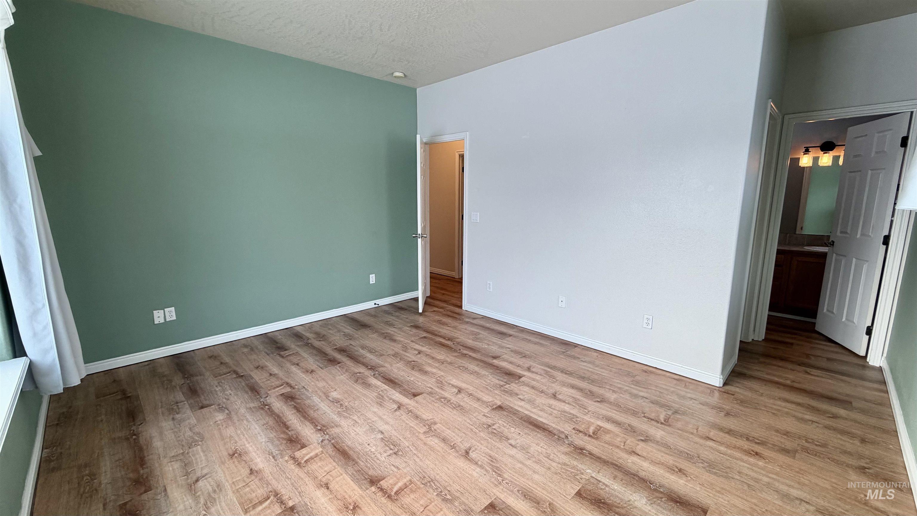 Unfurnished bedroom featuring light wood-style flooring, a textured ceiling, and ensuite bath