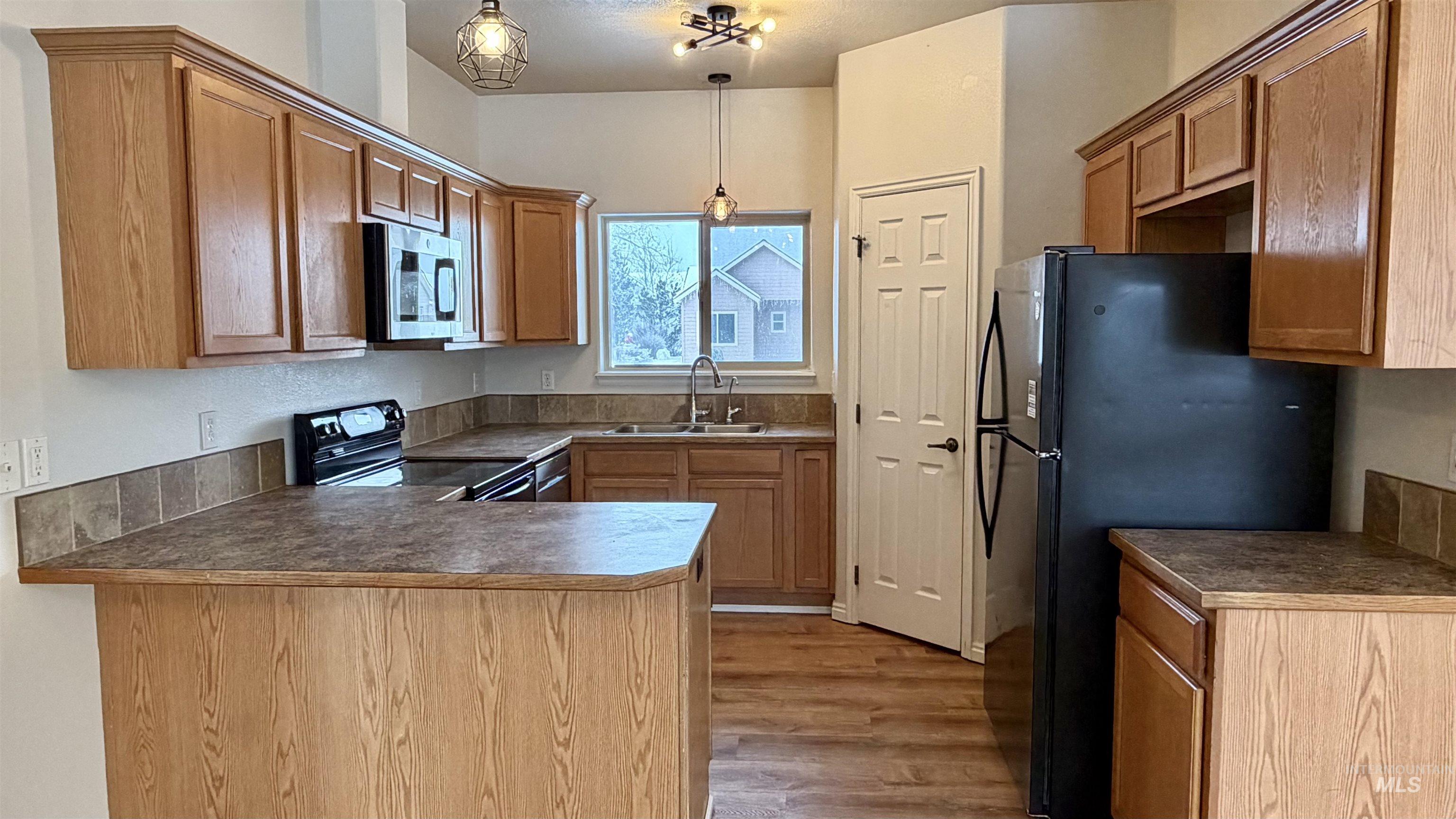 Kitchen featuring dark countertops, black appliances, pendant lighting, a peninsula, and brown cabinets