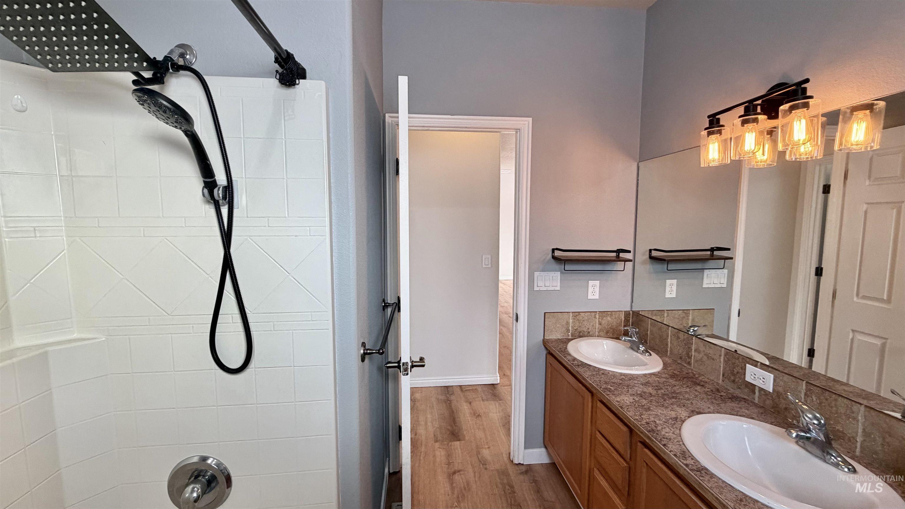 Bathroom with double vanity, dark wood-style floors, and tiled shower / bath