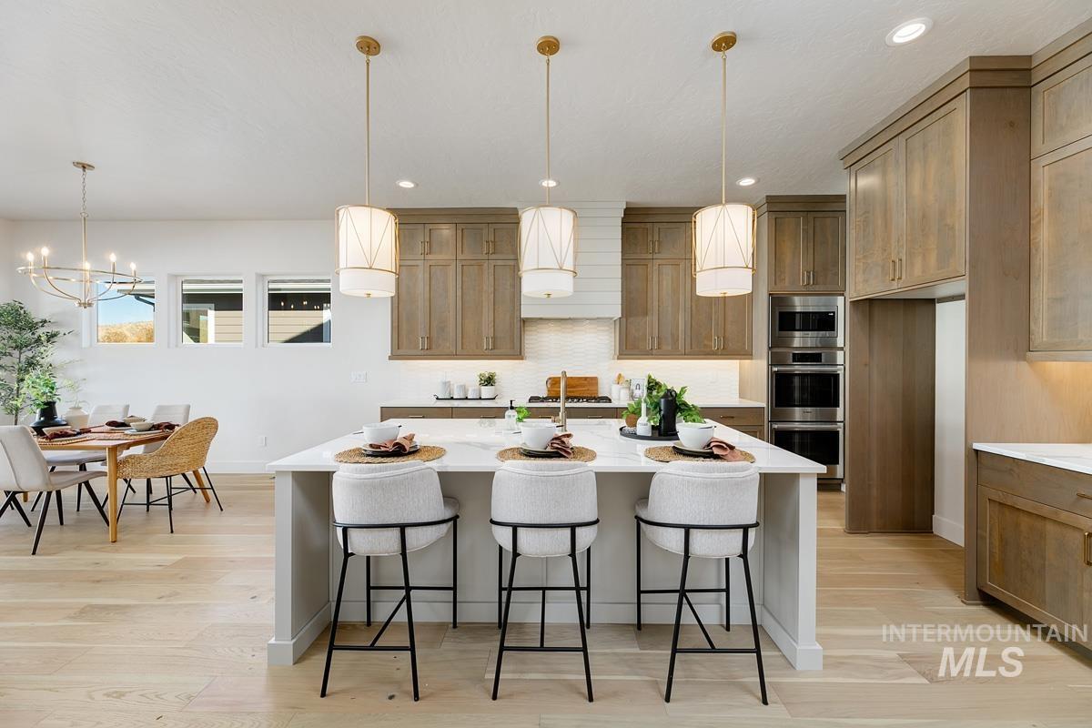 Kitchen with brown cabinets, a breakfast bar area, hanging light fixtures, a kitchen island with sink, and recessed lighting