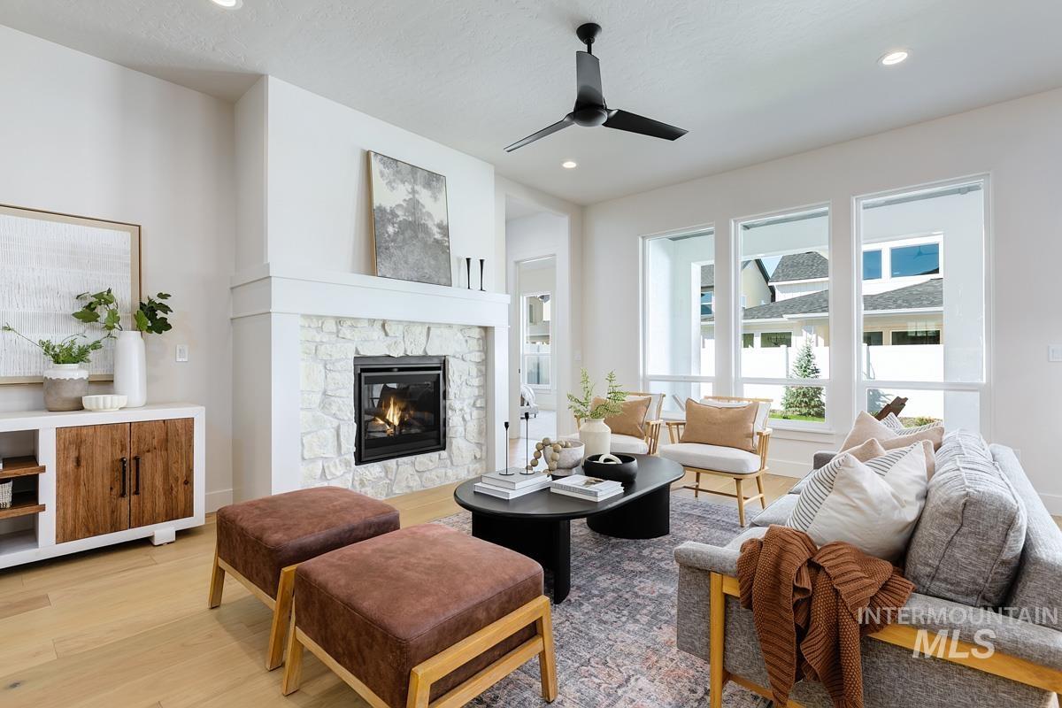 Living area featuring light wood-style floors, a stone fireplace, ceiling fan, and recessed lighting