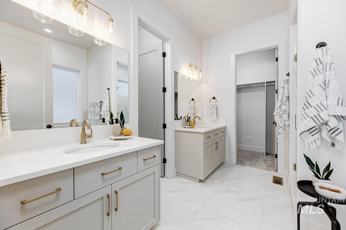 Bathroom with two vanities, light marble finish floors, and a walk in closet