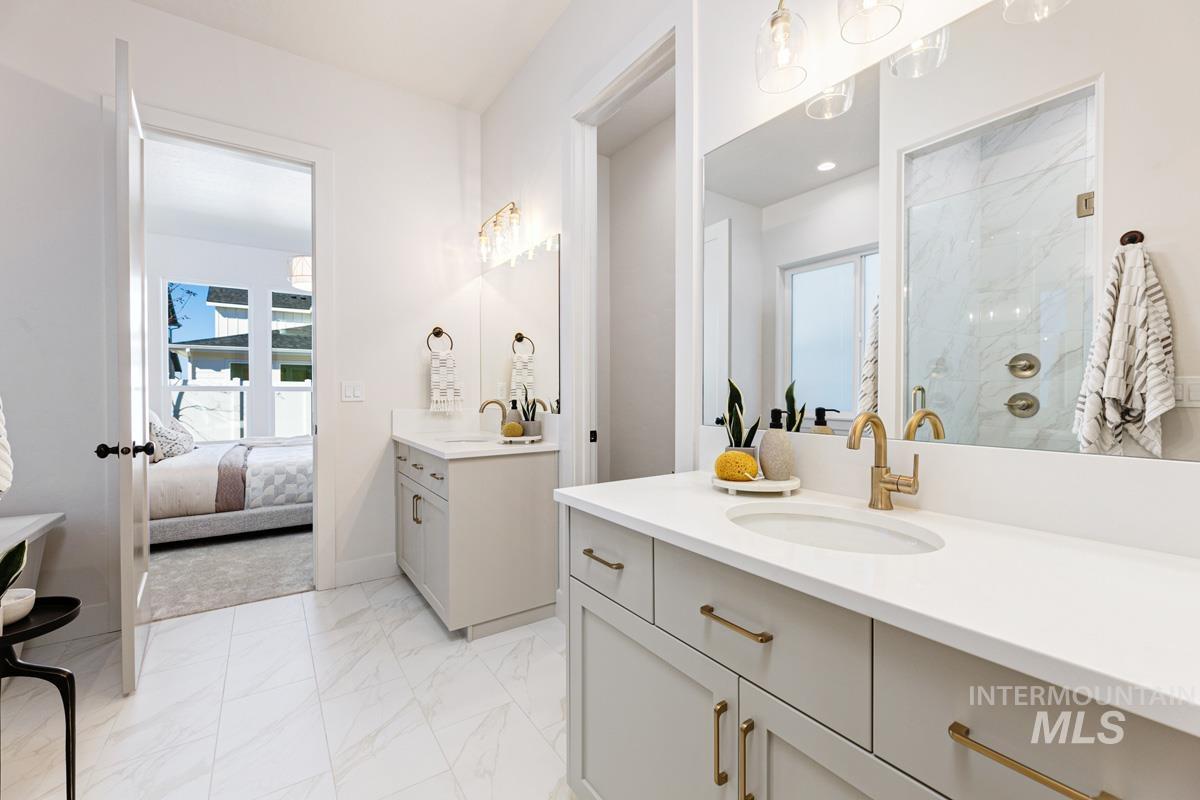 Ensuite bathroom with two vanities, light marble finish flooring, a marble finish shower, and plenty of natural light