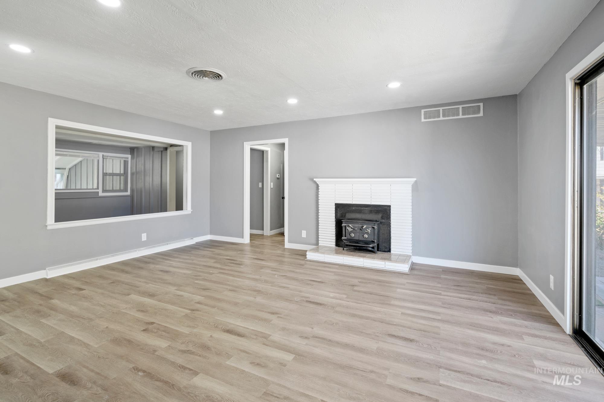 Unfurnished living room with a wood stove, light wood finished floors, recessed lighting, and a textured ceiling