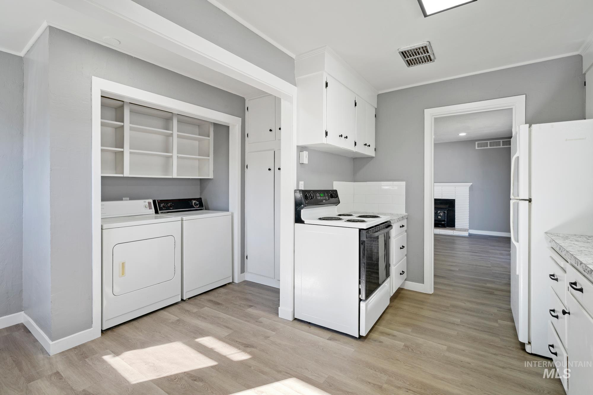Kitchen with white cabinetry, white appliances, light wood finished floors, washer and clothes dryer, and light countertops