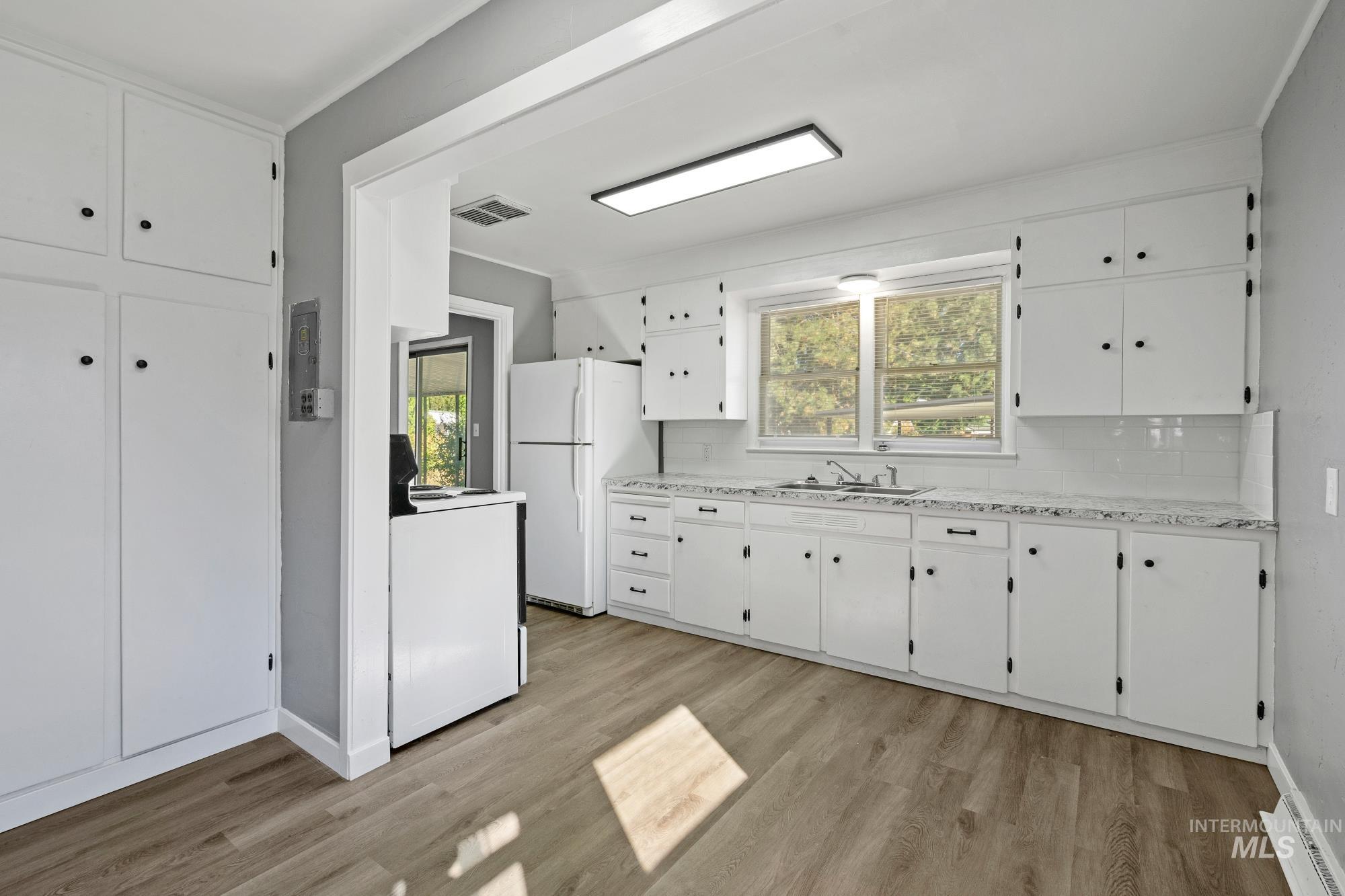 Kitchen with white appliances, white cabinetry, light wood-style flooring, and backsplash