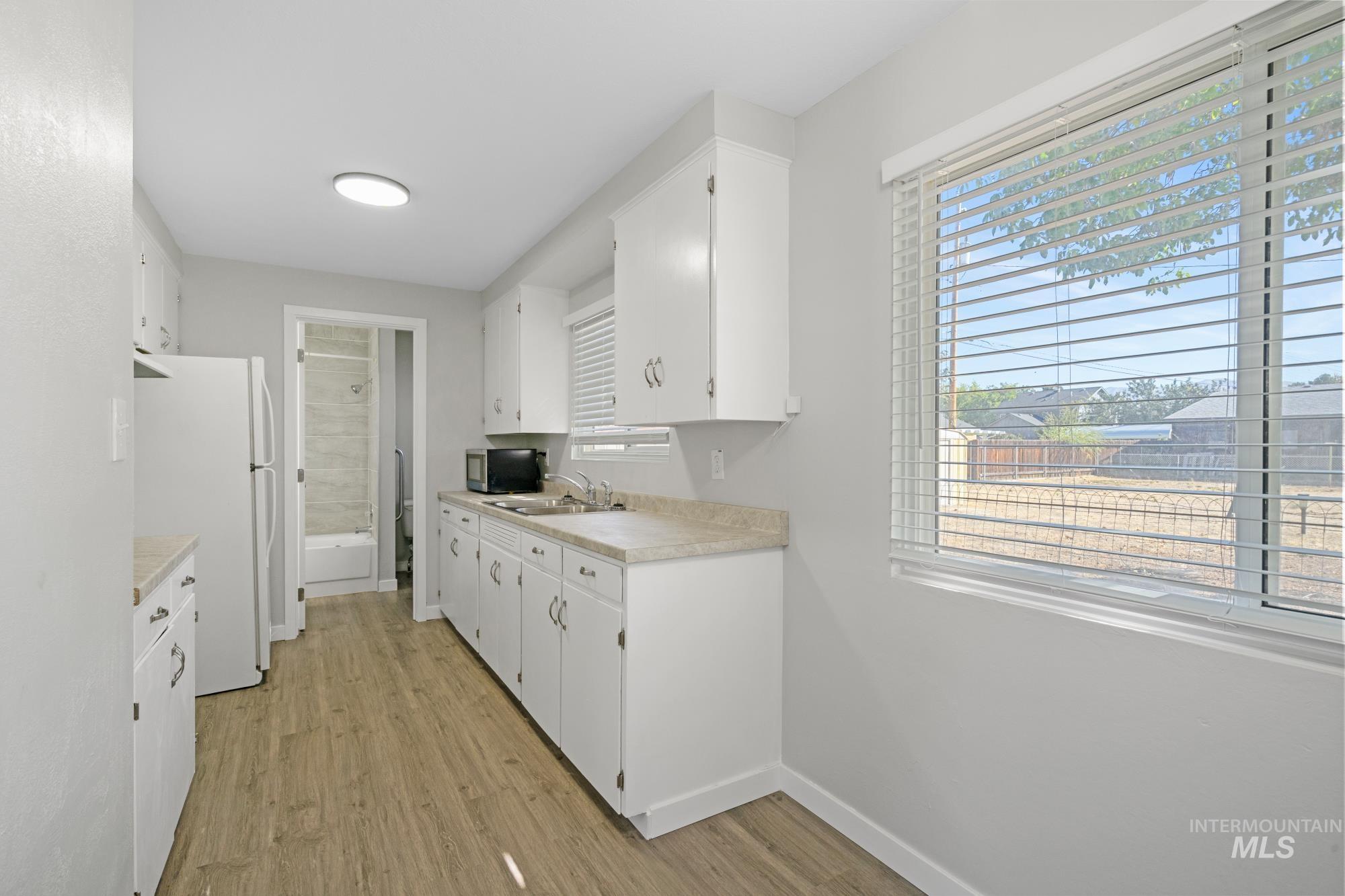 Kitchen with freestanding refrigerator, light wood-style floors, light countertops, and white cabinetry