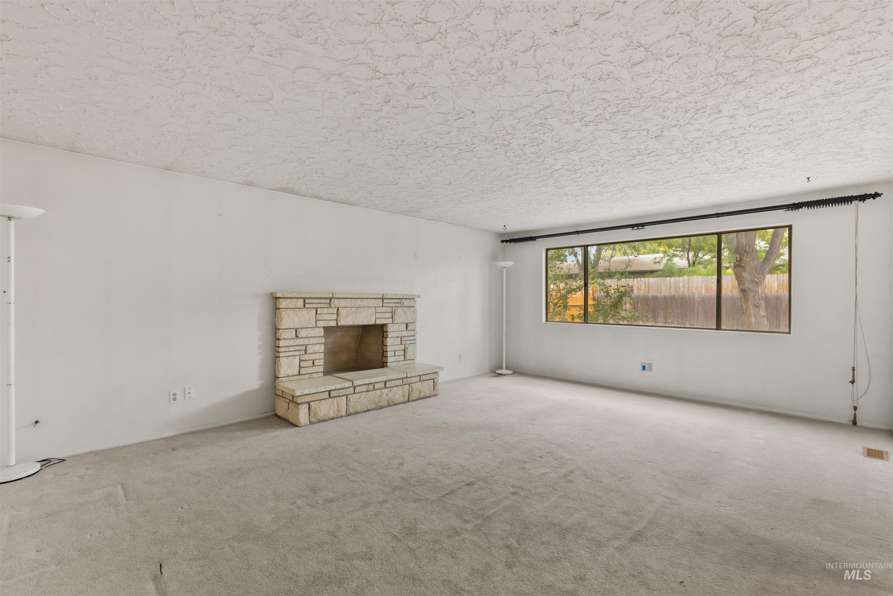 Unfurnished living room with a stone fireplace, carpet, and a textured ceiling