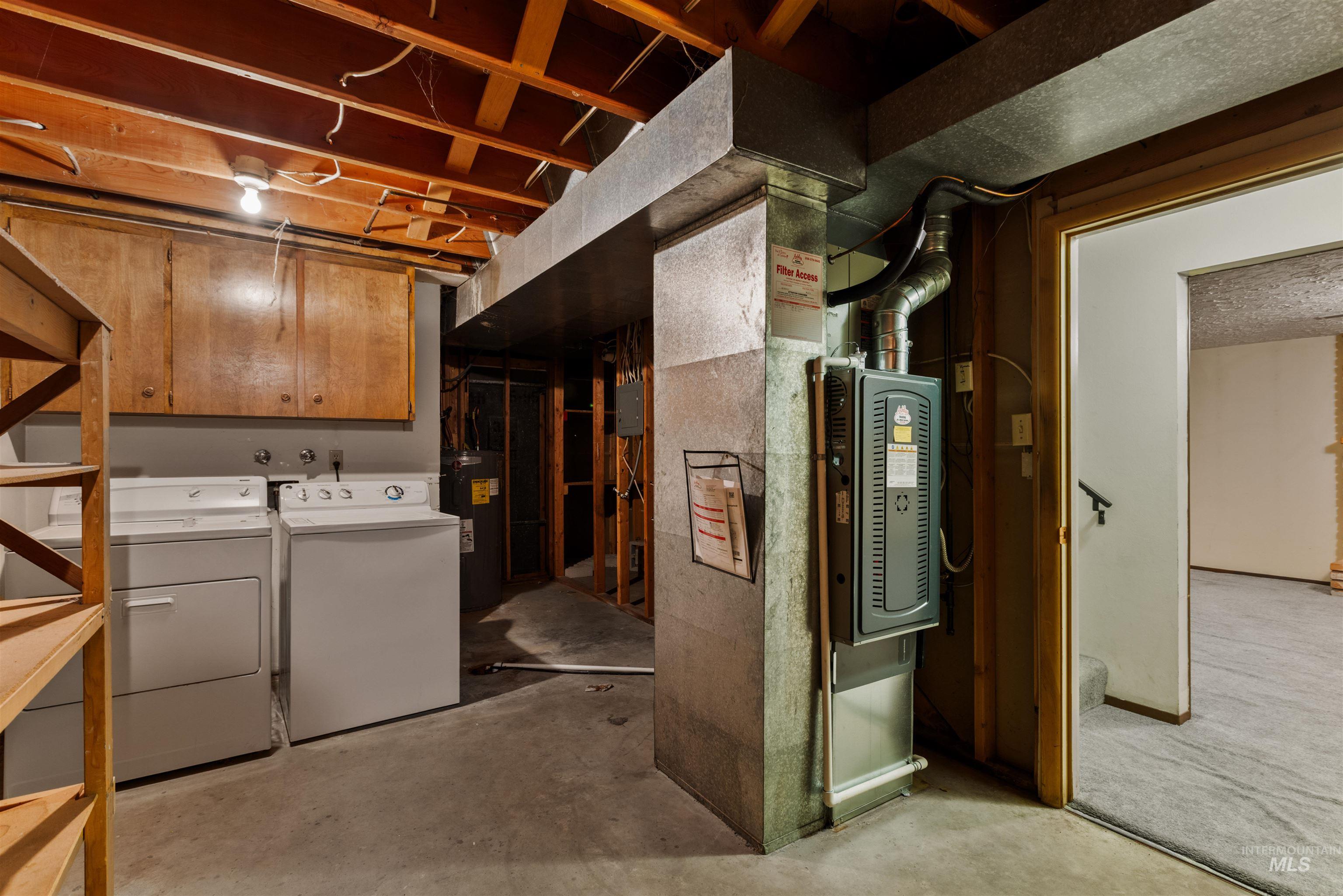 Unfinished below grade area featuring electric water heater, heating unit, and washer and dryer