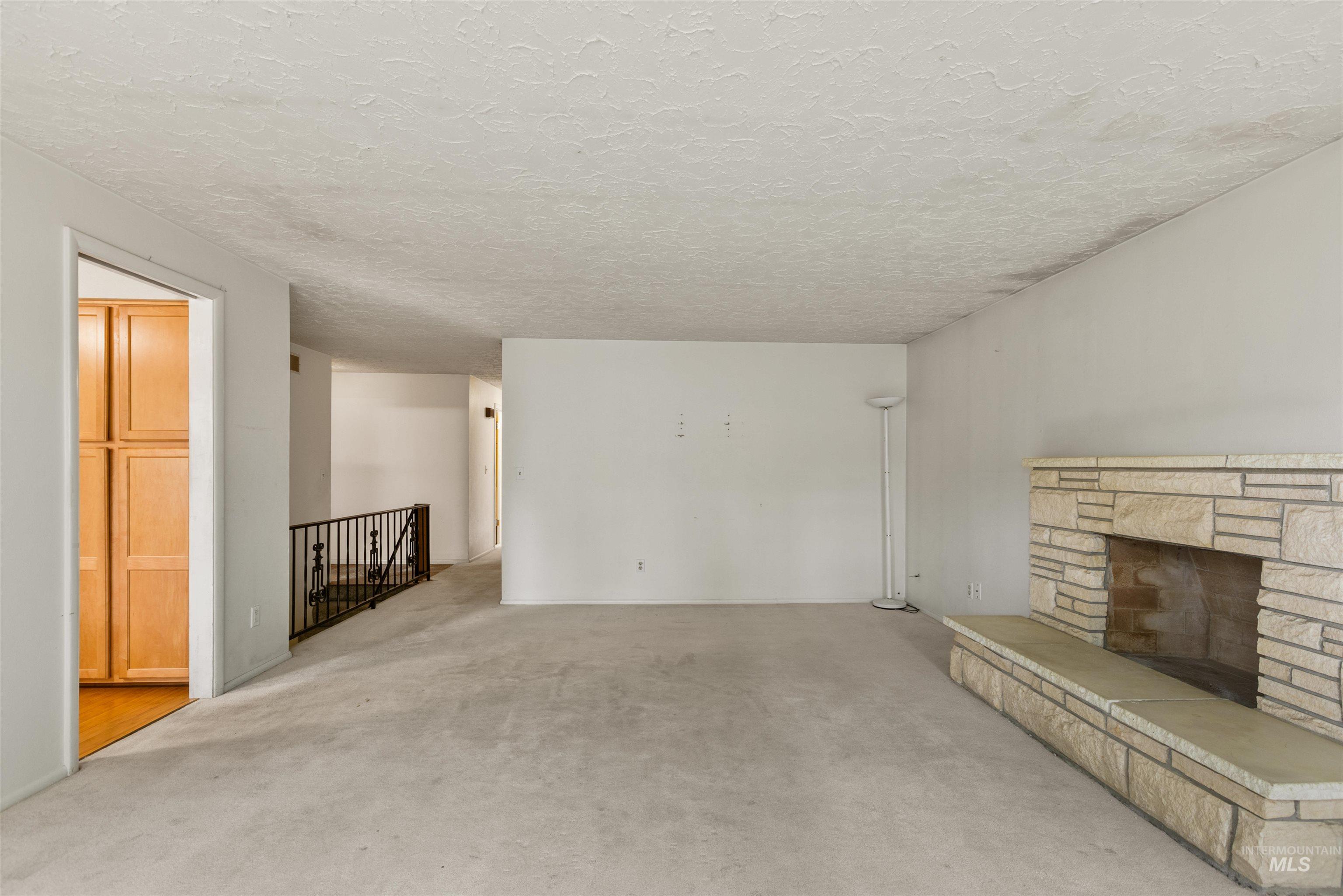 Unfurnished living room with a stone fireplace, carpet, and a textured ceiling