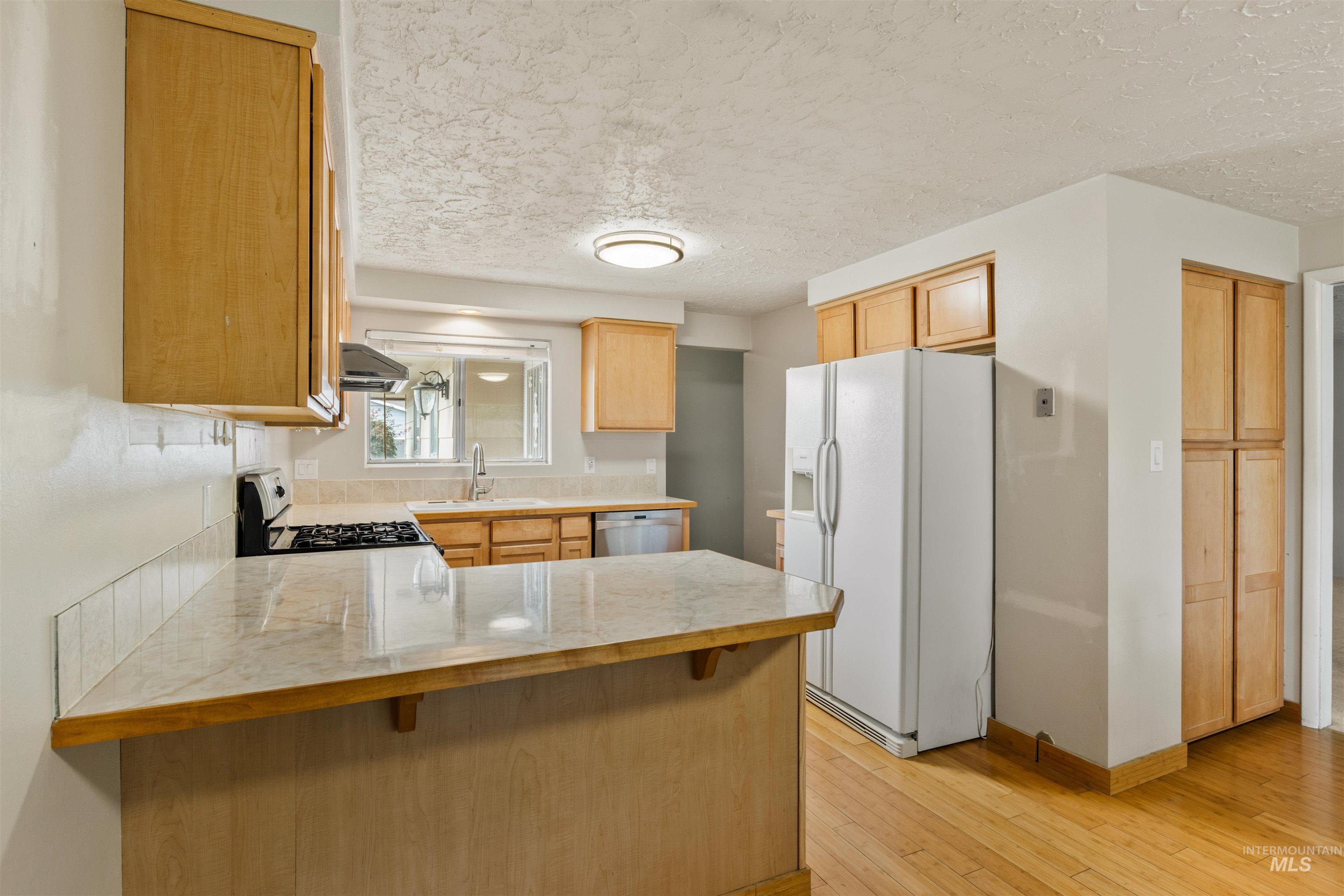 Kitchen featuring a peninsula, white fridge with ice dispenser, a breakfast bar, light wood-style flooring, and a textured ceiling