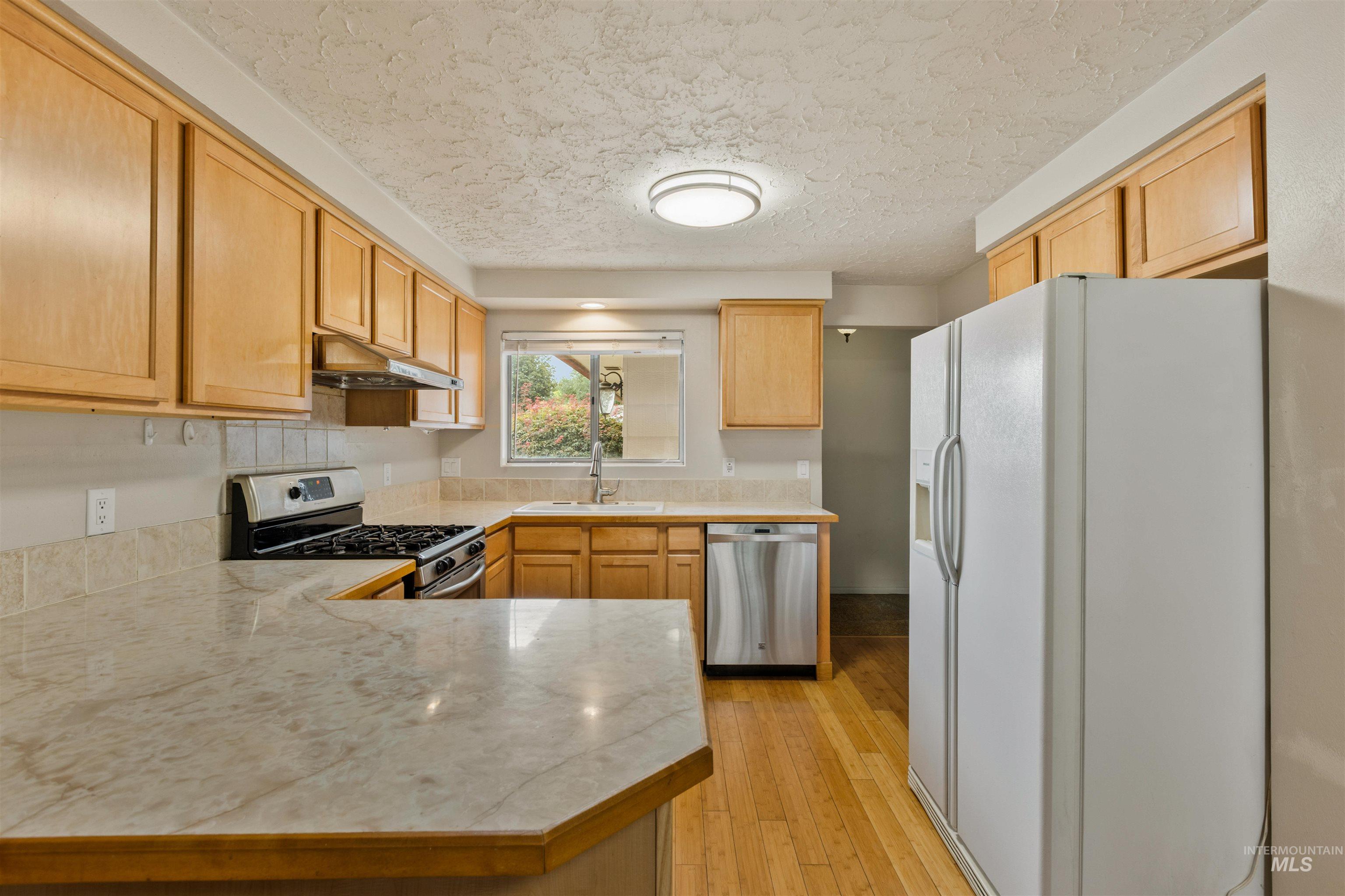 Kitchen with stainless steel appliances, a textured ceiling, light wood-style floors, a peninsula, and under cabinet range hood