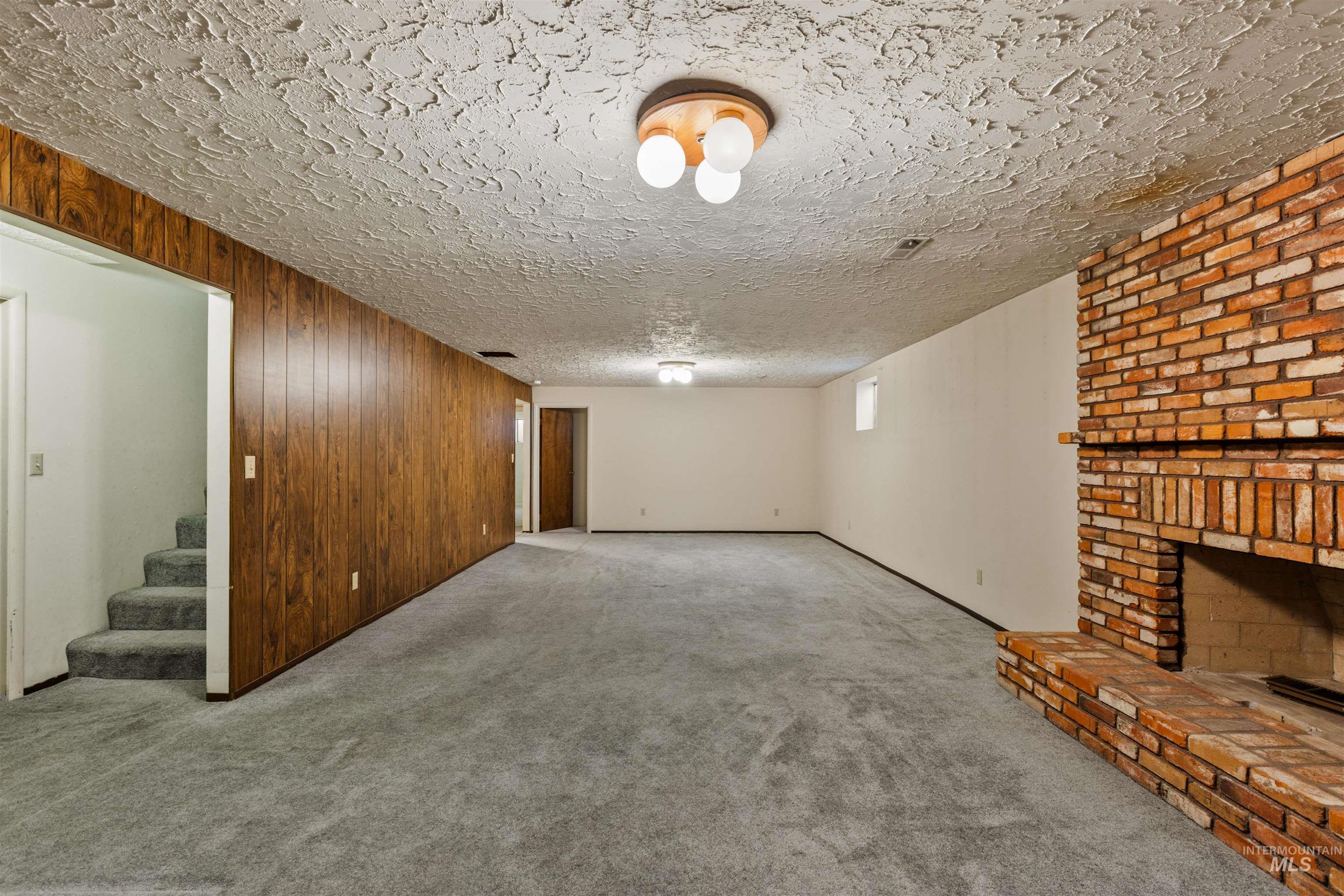 Basement with wood walls, carpet flooring, a fireplace, a textured ceiling, and stairs