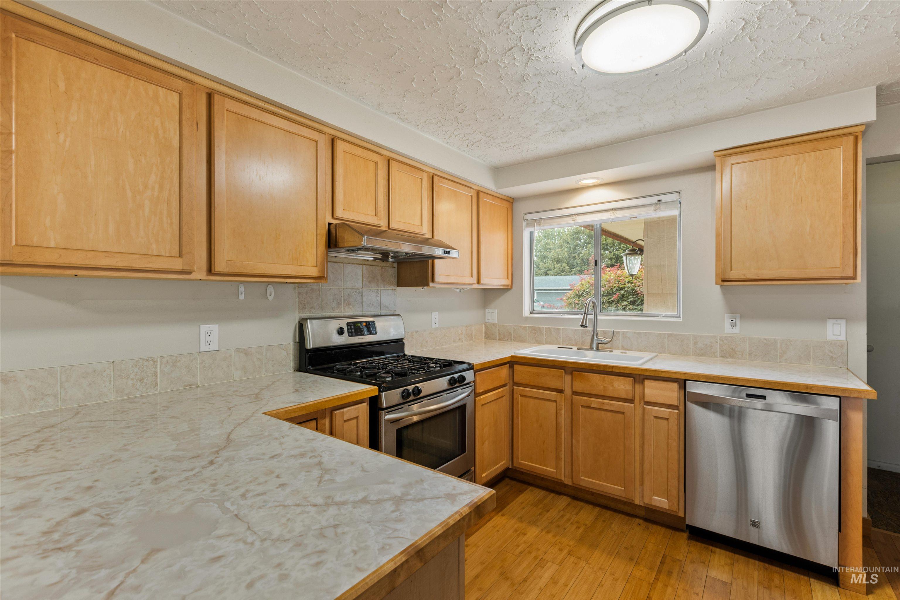 Kitchen featuring stainless steel appliances, light wood finished floors, a textured ceiling, and under cabinet range hood