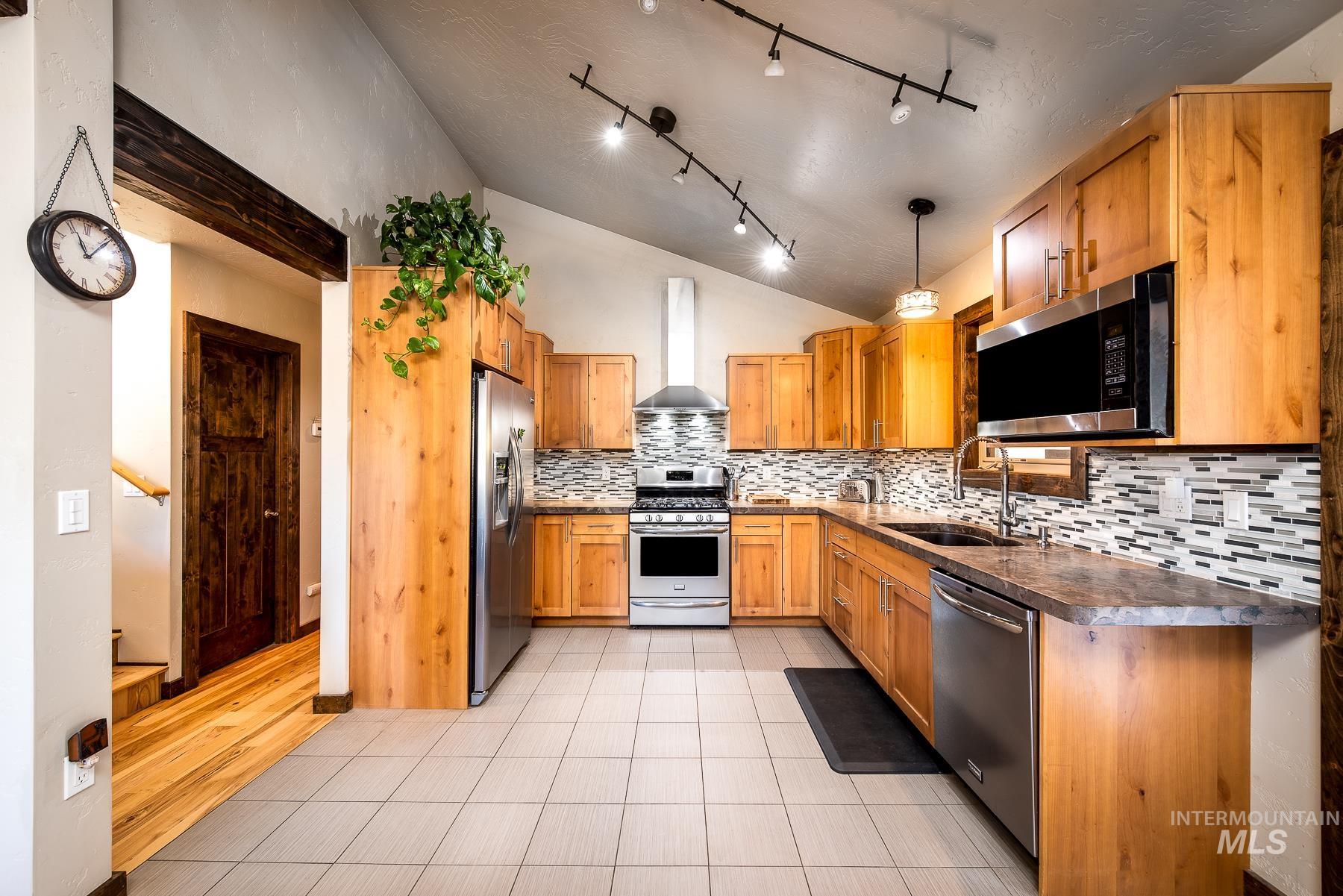 Kitchen featuring dark countertops, stainless steel appliances, light tile patterned floors, lofted ceiling, and backsplash