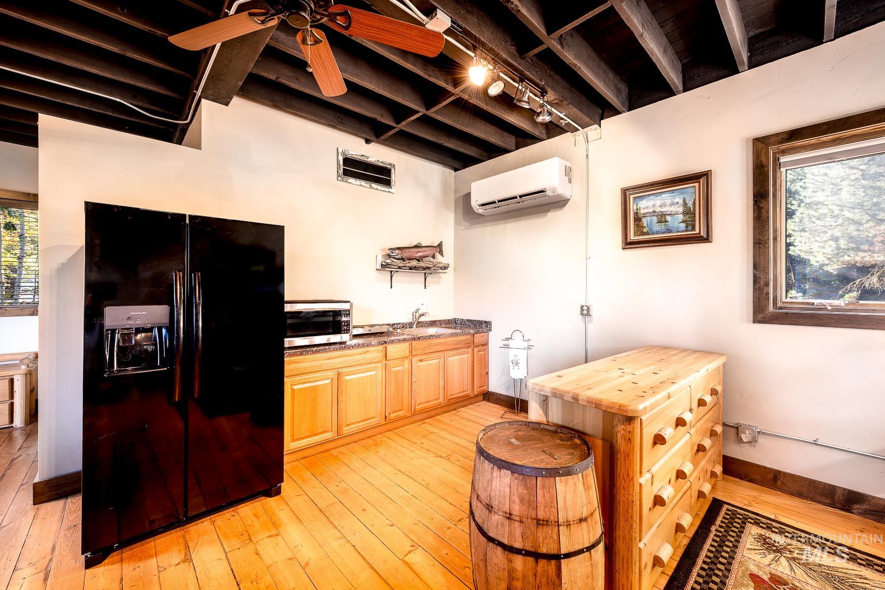 Kitchen featuring black refrigerator with ice dispenser, a ceiling fan, stainless steel microwave, light wood-type flooring, and wood counters